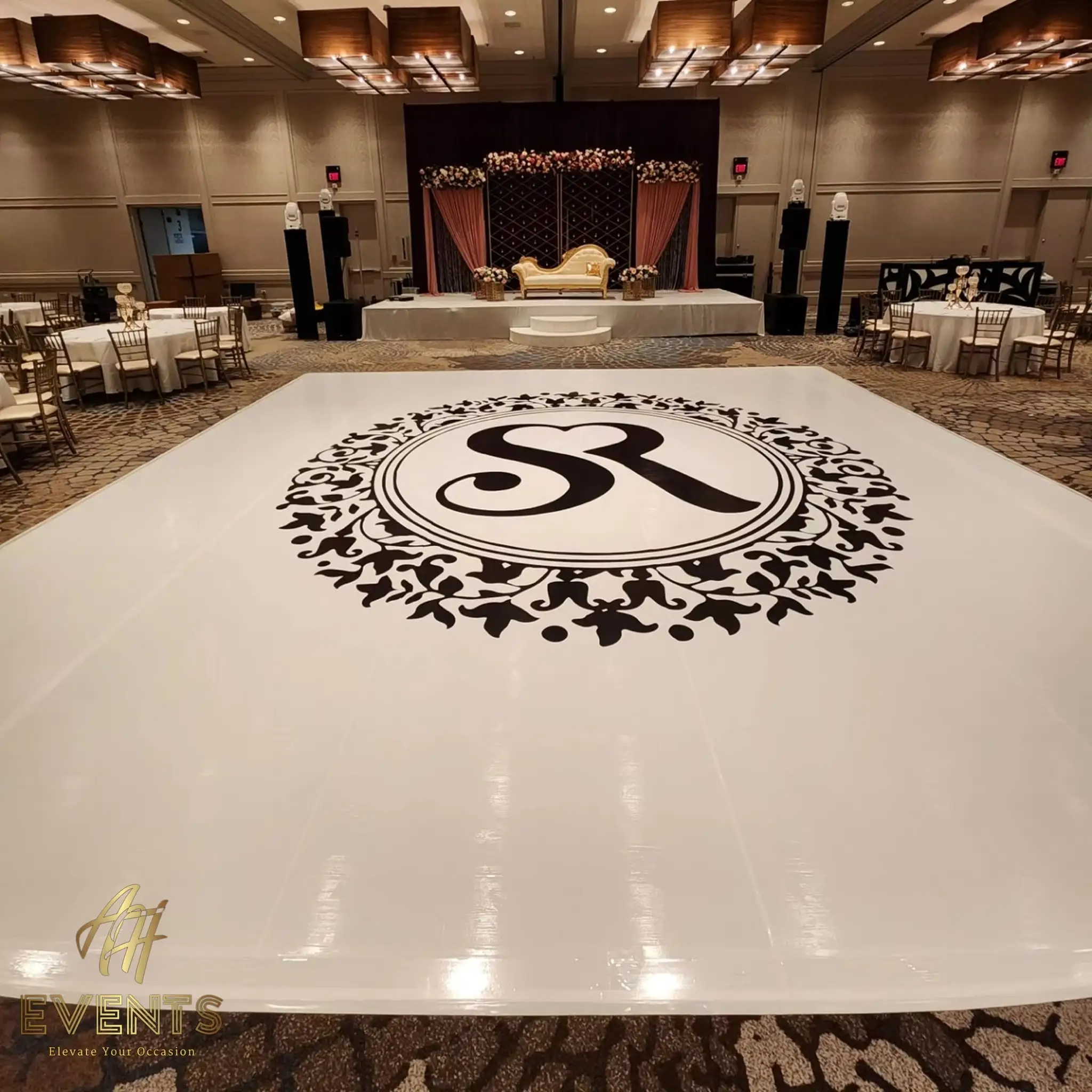 Glossy white dance floor with an ornate 'SR' floral-roundel monogram, facing a mauve-draped stage with a gold sofa