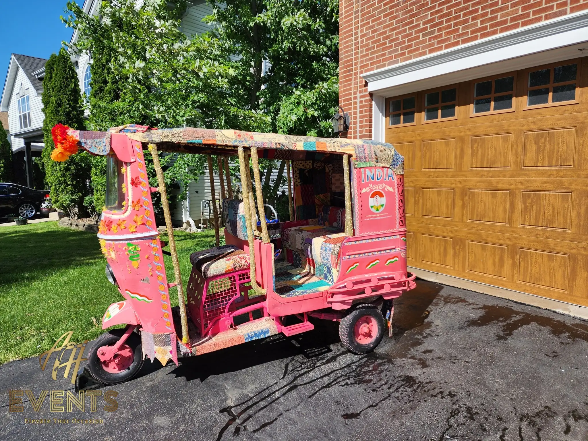 Restored pink auto rickshaw with patchwork upholstery parked in a driveway, before event decoration