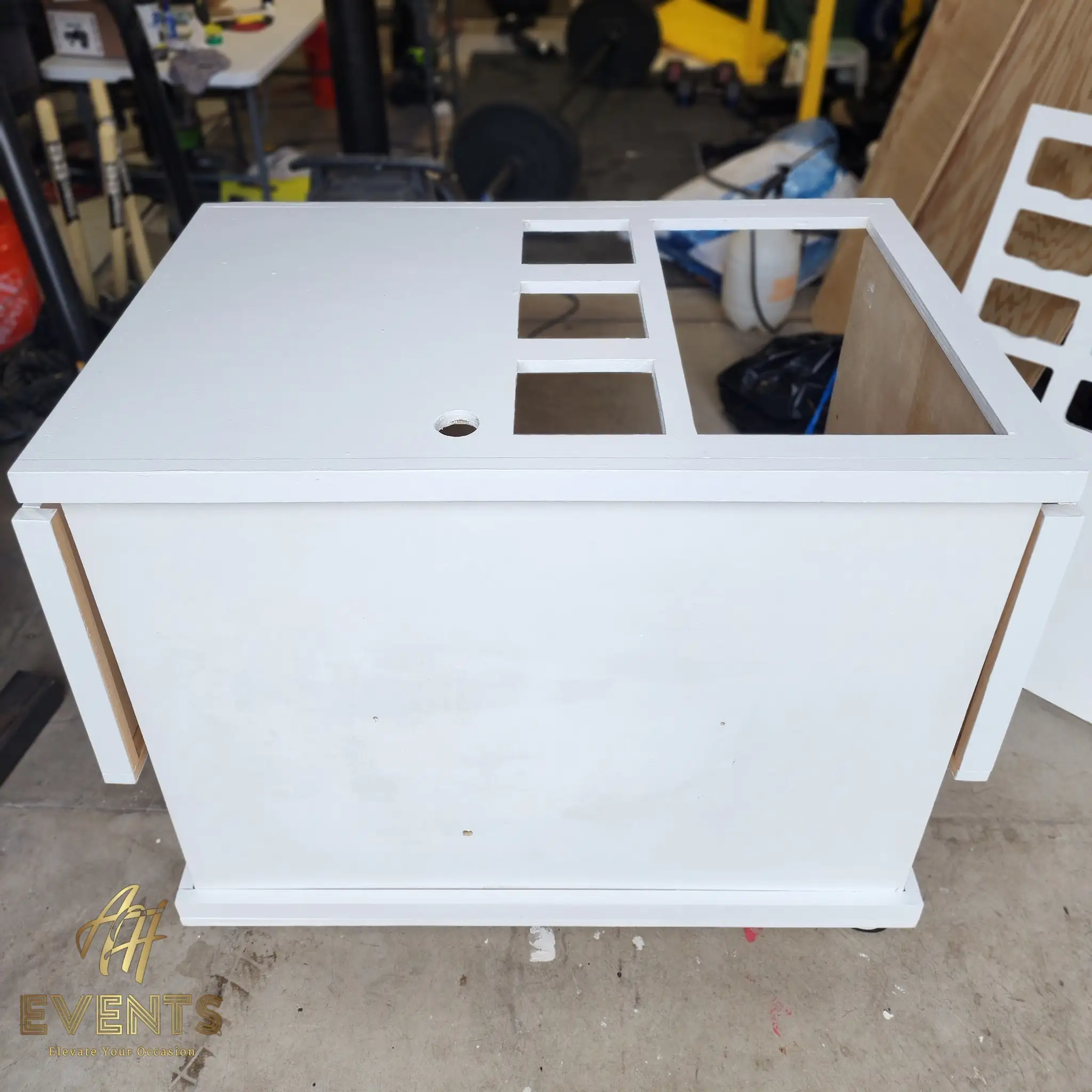 Primed white cart-top box in the workshop with a column of square cut-out wells, a large open well and a round hole