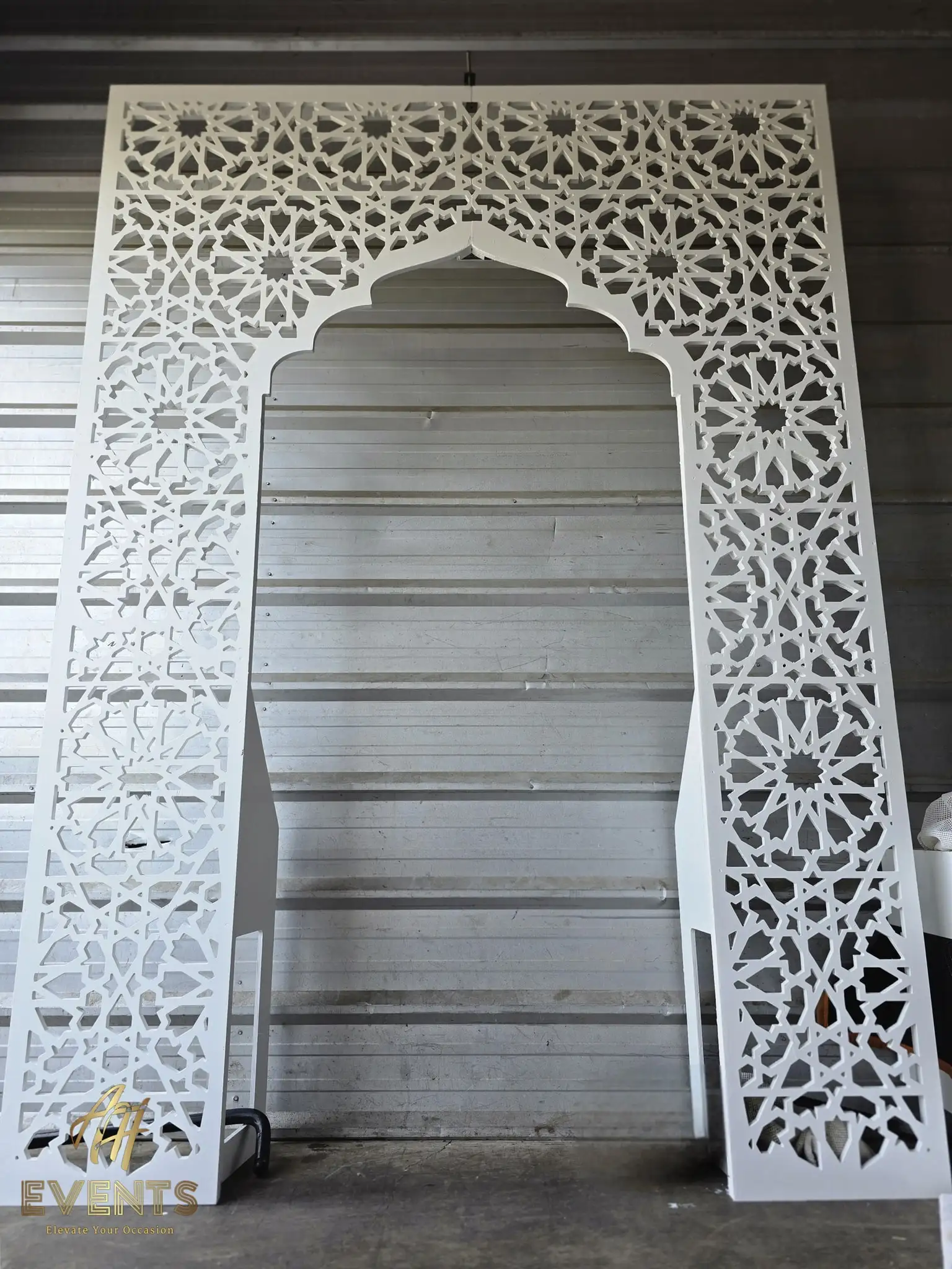 White semi-gloss star-lattice Mughal arch leaning against a corrugated metal wall in the workshop