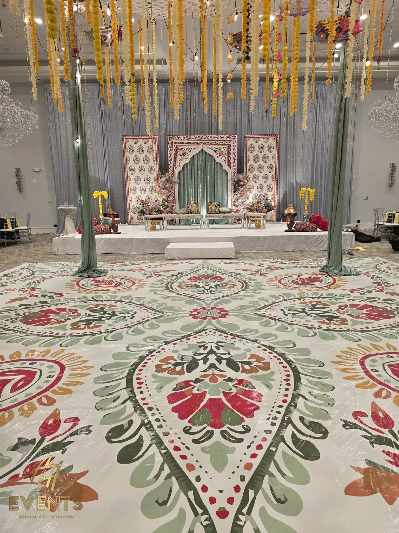 Floral flex vinyl dance floor with medallion and paisley patterns in a banquet hall, framed by sage-green draped pillars and a decorated stage