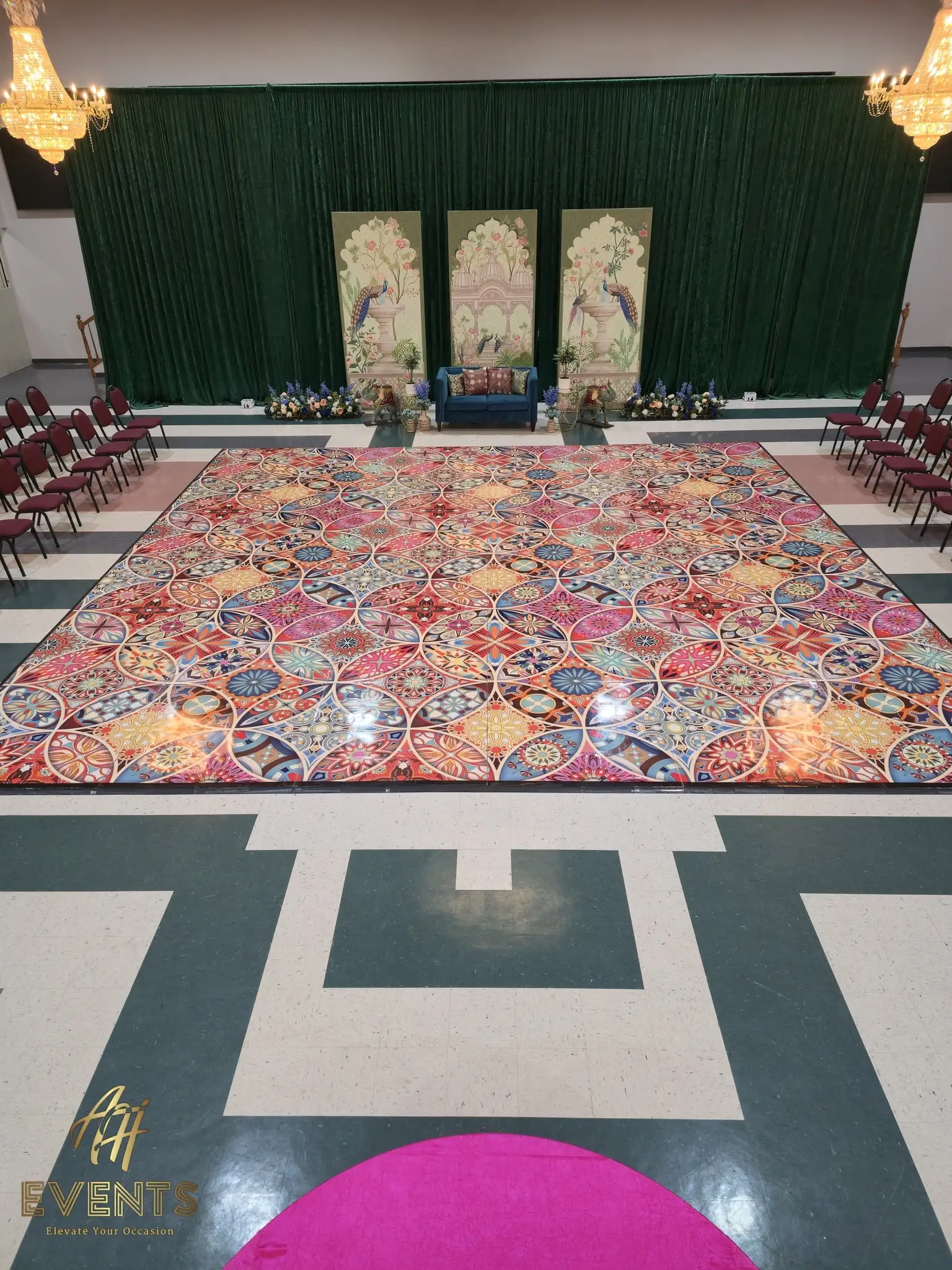 Aerial view of a Kaleidoscope decorative floor in a banquet hall, with a green-draped stage and peacock-print panels