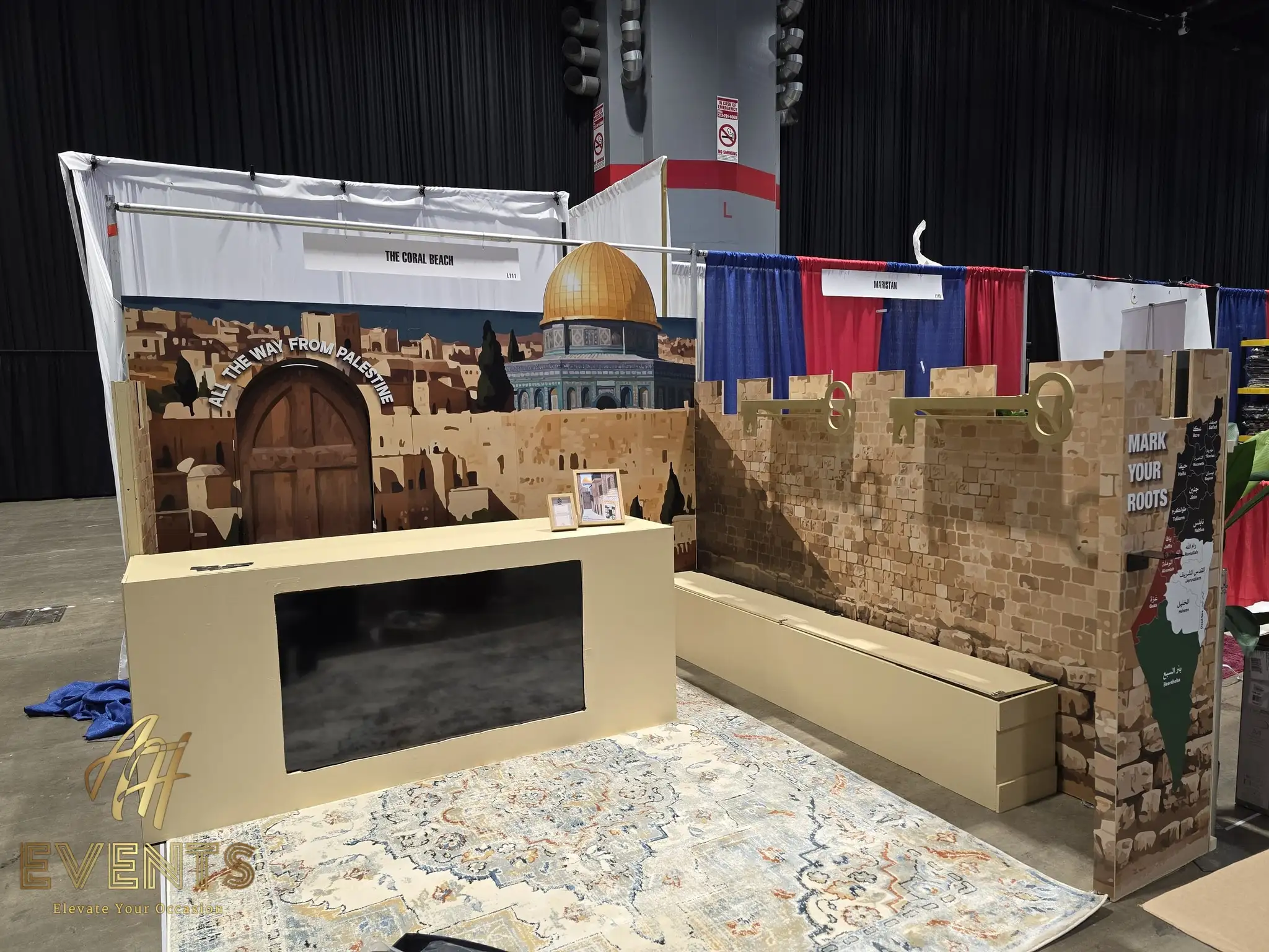 The Coral Beach convention booth with a Jerusalem mural, the Dome of the Rock, a wooden door and a counter with a TV cut-out