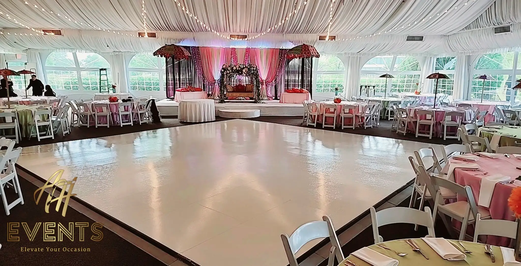 White dance floor in a glass-walled tent with a draped white ceiling, facing a pink stage in daylight