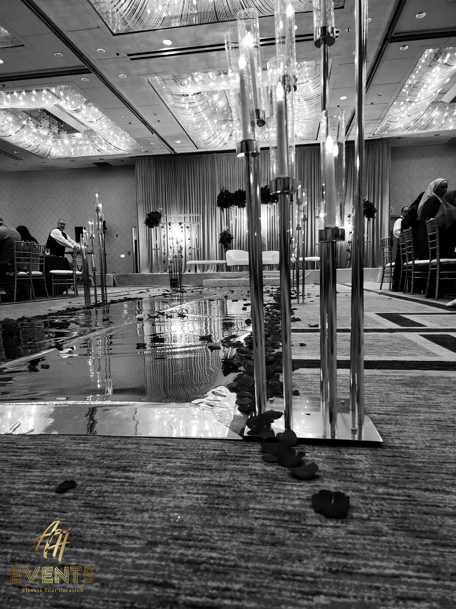 Reflective mirror vinyl aisle lined with tall crystal candelabras and scattered rose petals, in black and white
