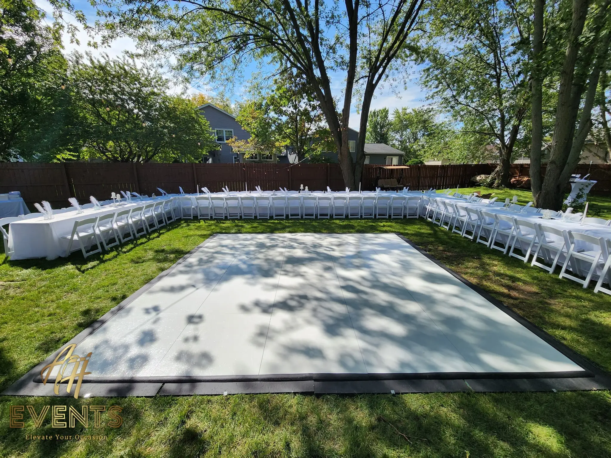 White dance floor set on a sunny backyard lawn with white folding chairs arranged around it