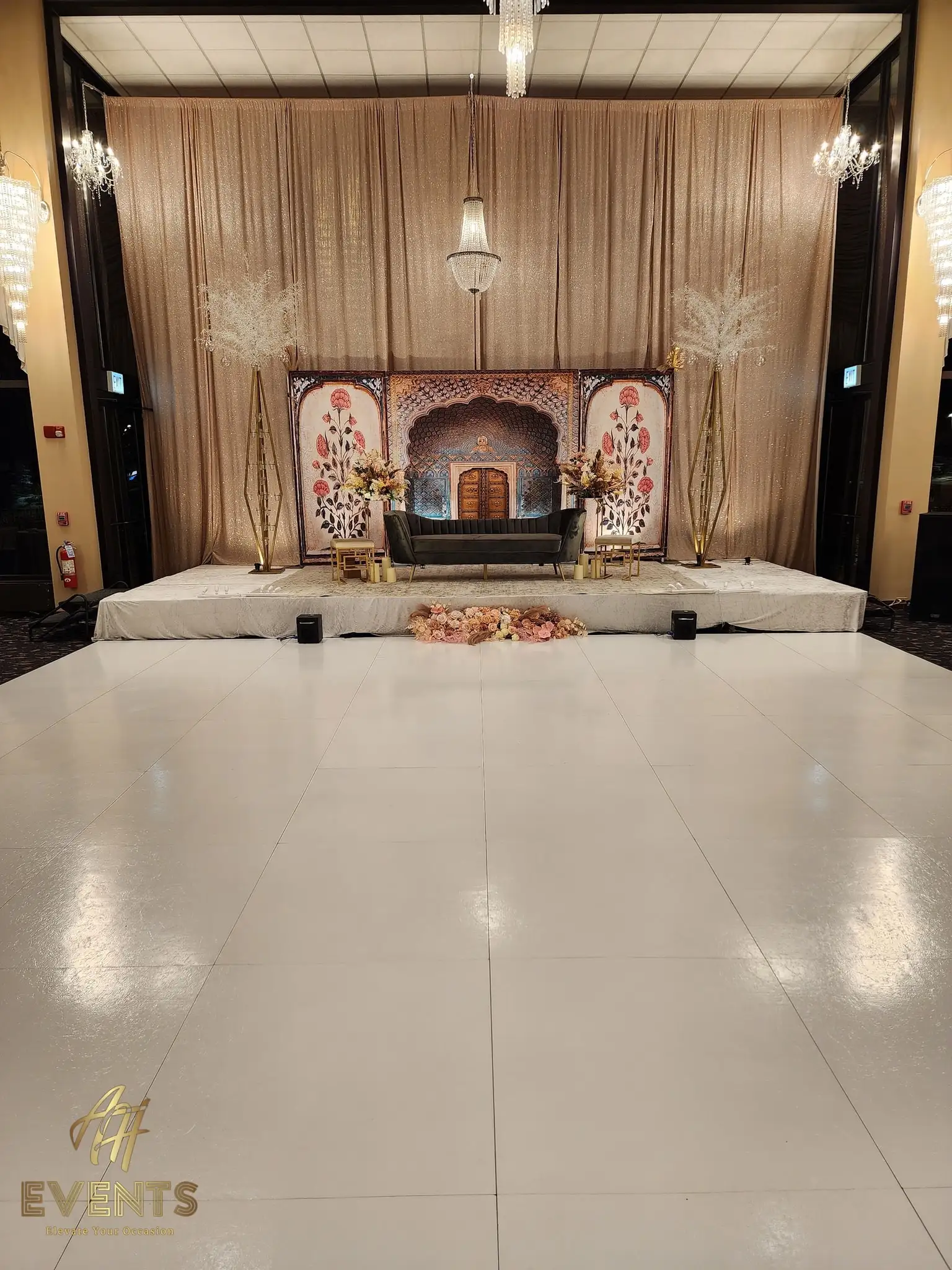 White dance floor before a beige-draped Mughal-style stage with a gray sofa and floral side panels