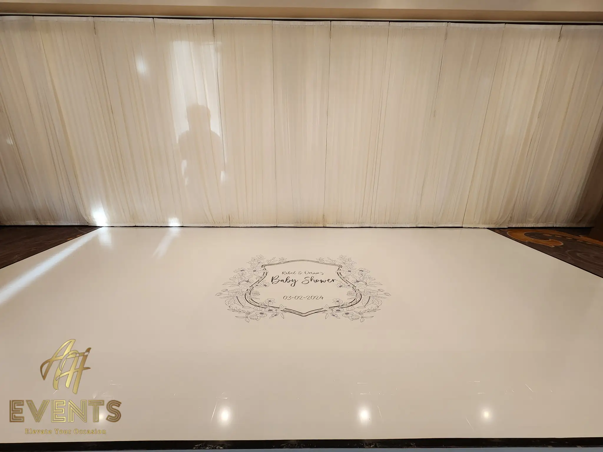 Cream dance floor with the floral-crest baby shower decal against a cream pleated drape