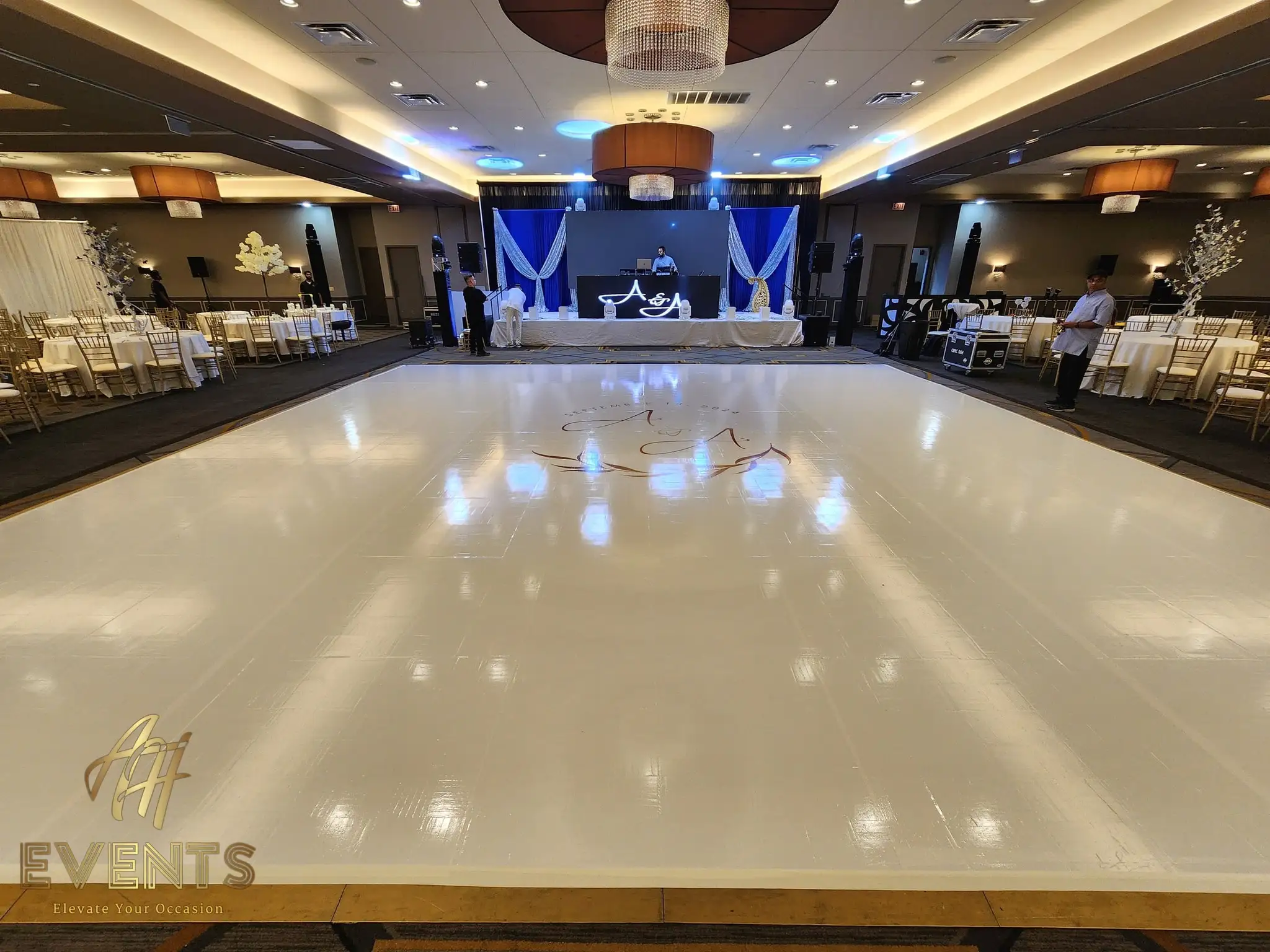 Wide ballroom view of the white 'A & A' monogram dance floor before a navy-draped stage and head table