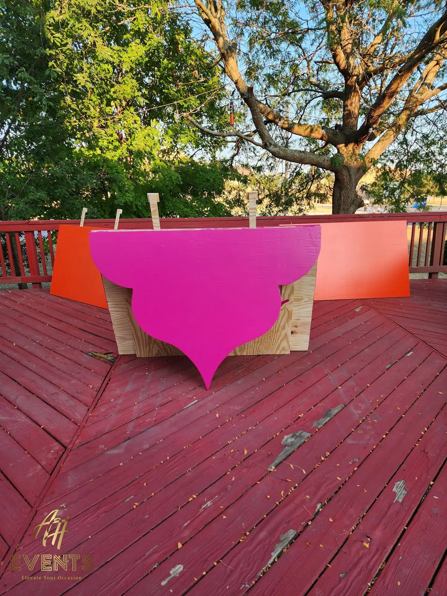 A magenta scalloped arch panel clamped to a plywood base during fabrication on the red deck, an orange panel behind