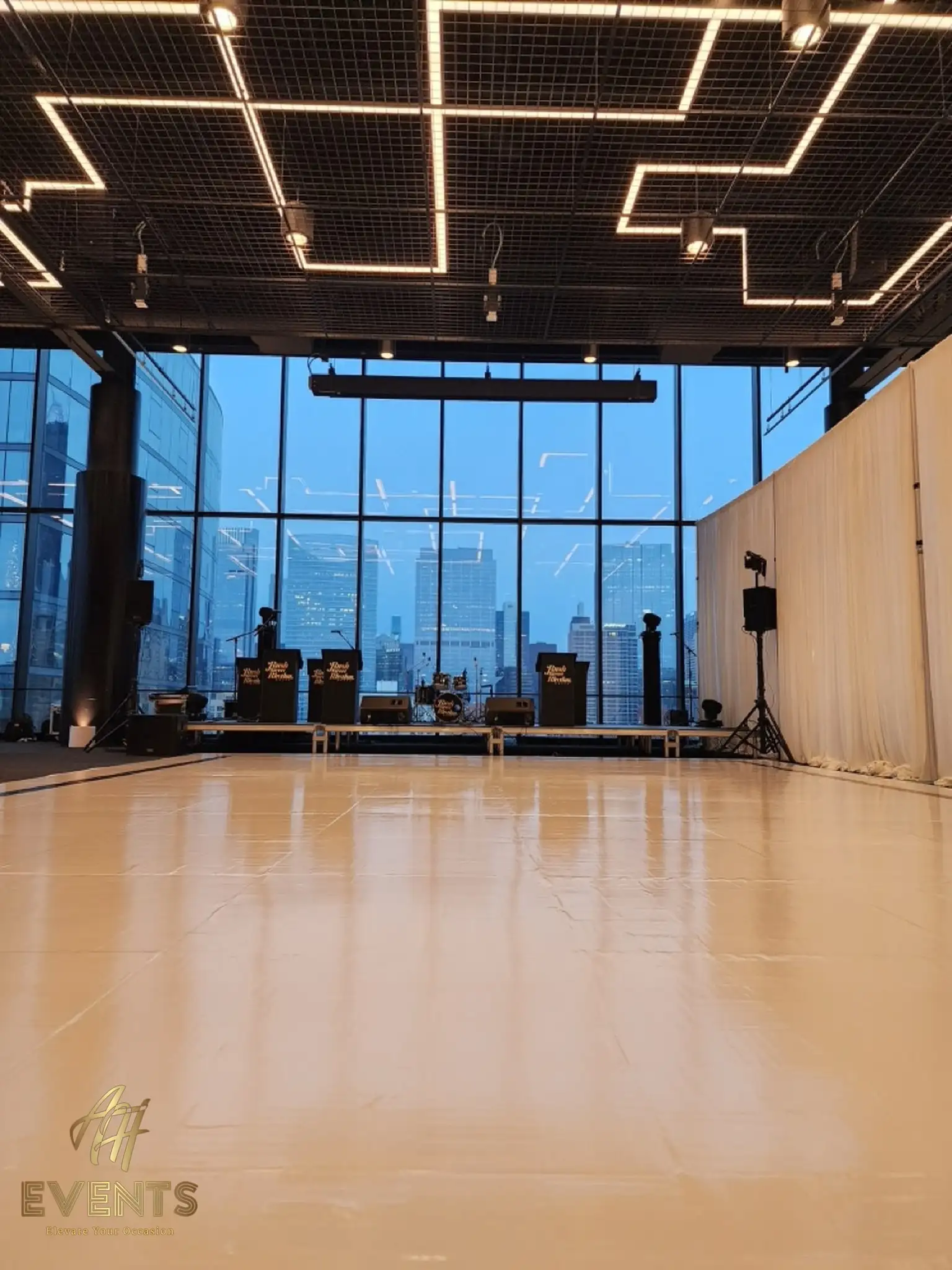 White dance floor in a skyline-windowed loft with a band stage, viewed across its glossy surface