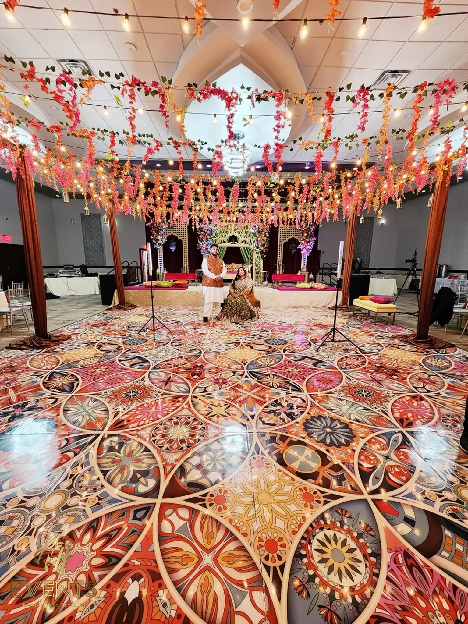 Kaleidoscope floor under a canopy of hanging florals and fairy lights, with a decorated stage behind