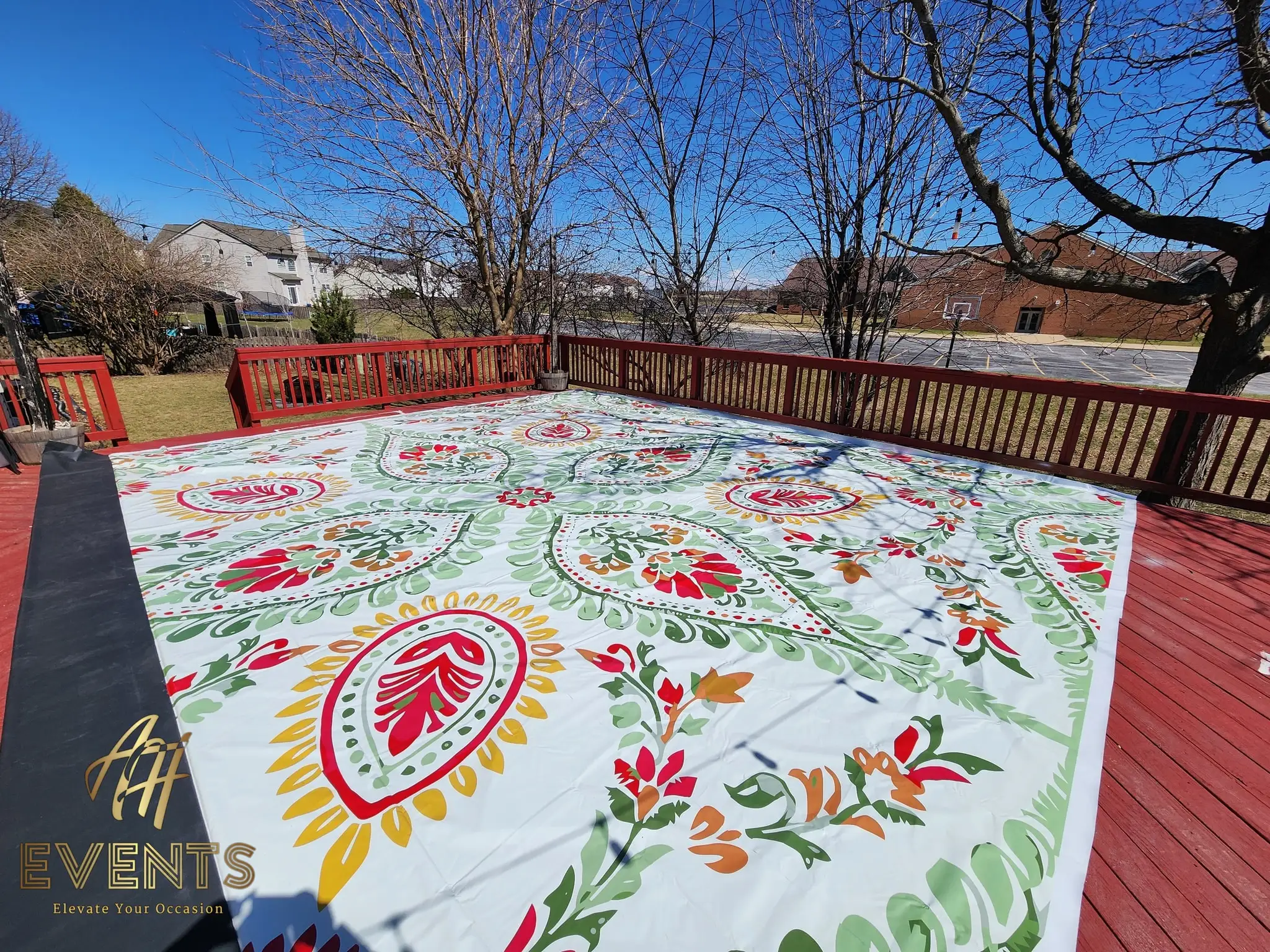 White flex vinyl floor with red and green paisley print laid out on an outdoor wooden deck under a clear blue sky