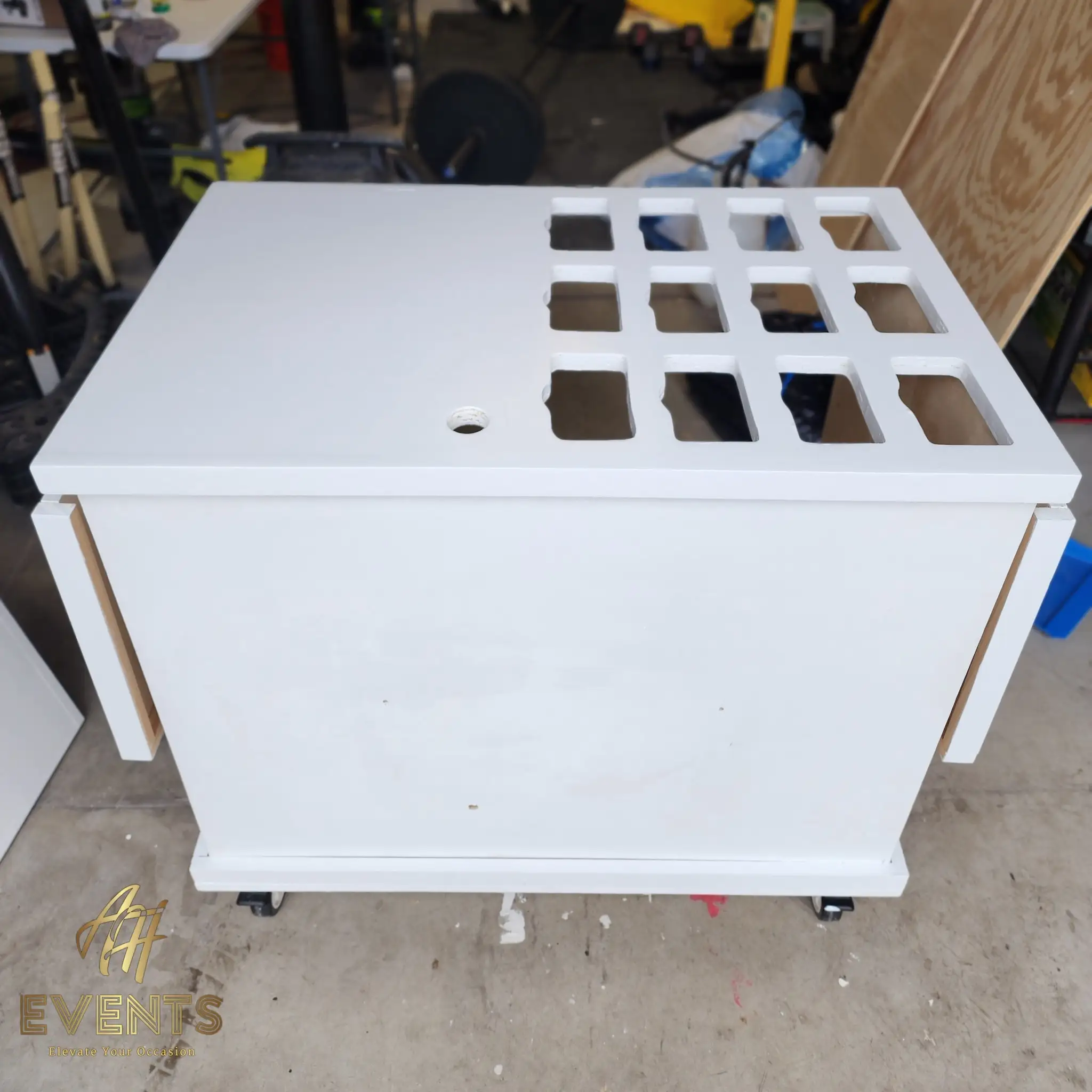 White cart-top box on casters with a grid of square cup-well cut-outs and a round hole, in the workshop