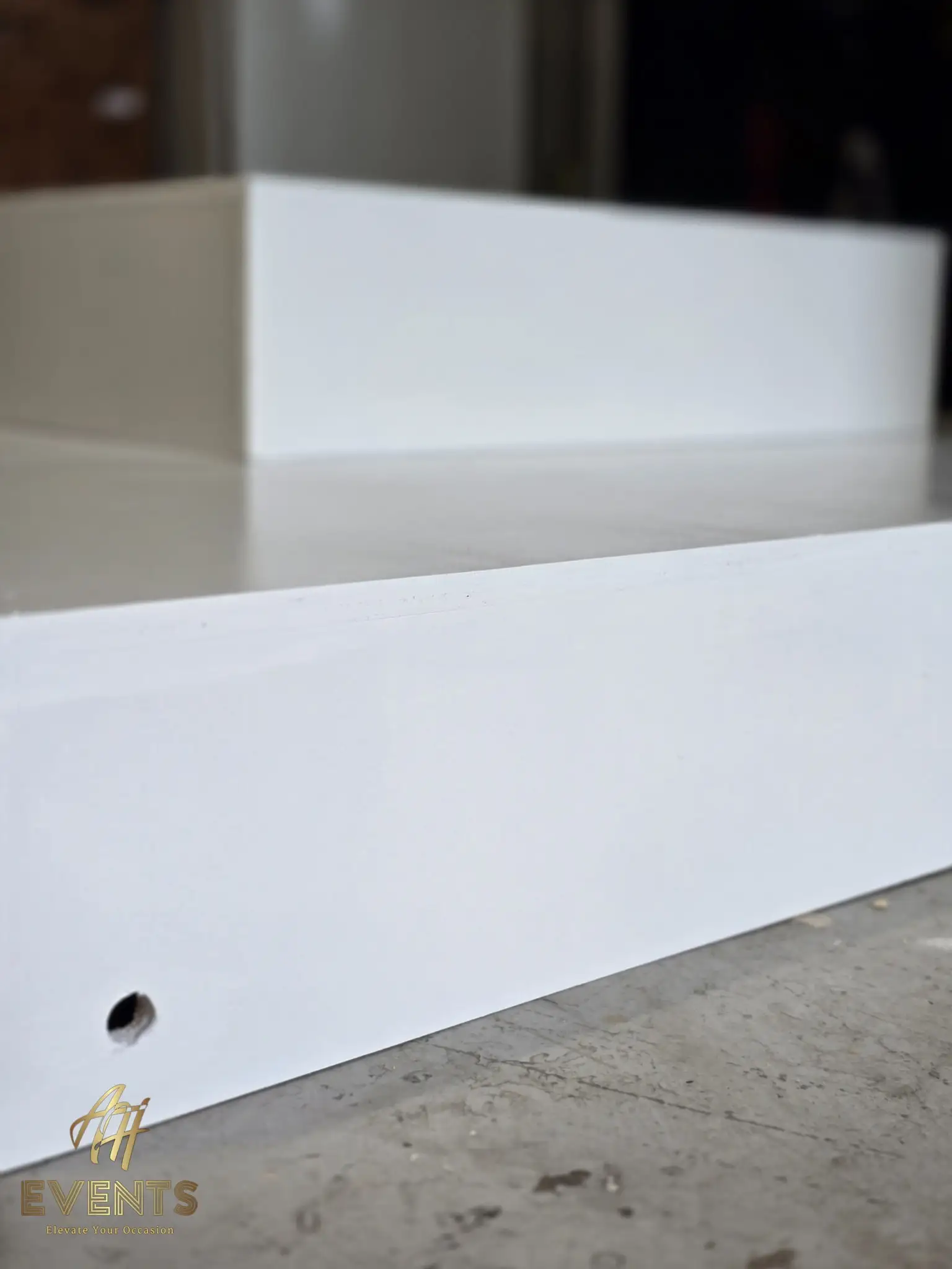 Close-up of a crisp white-painted platform edge with a drilled hole, a second riser behind