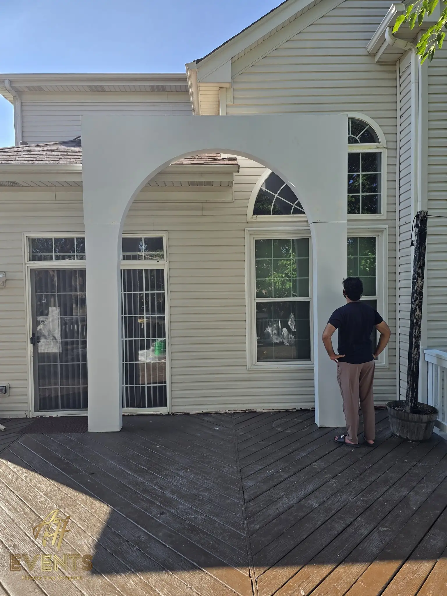 Single white volumetric arch against a house wall, with a person inspecting it on a deck