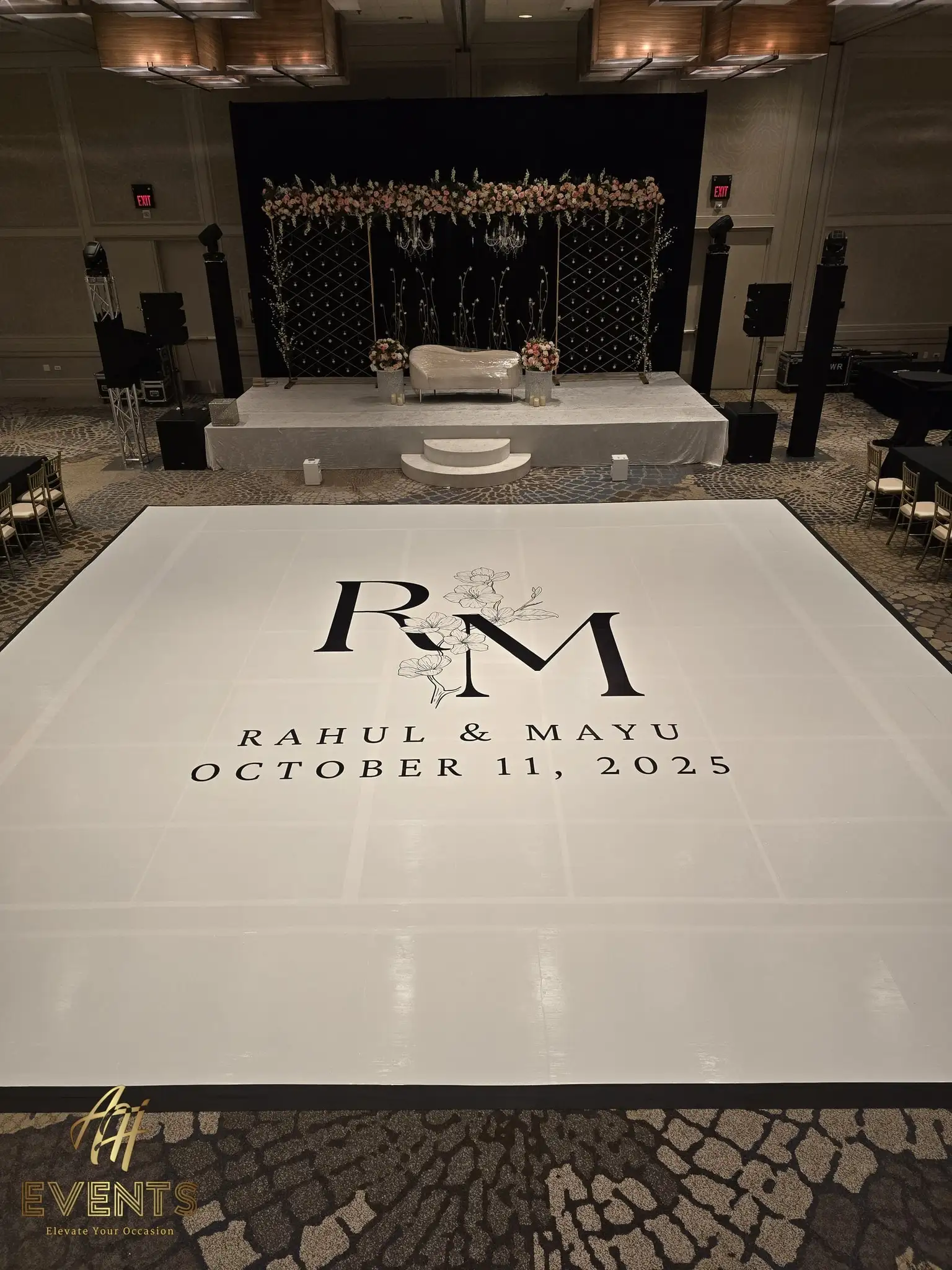 White 'R M' magnolia monogram dance floor facing a black diamond-lattice stage with a floral garland and cream settee