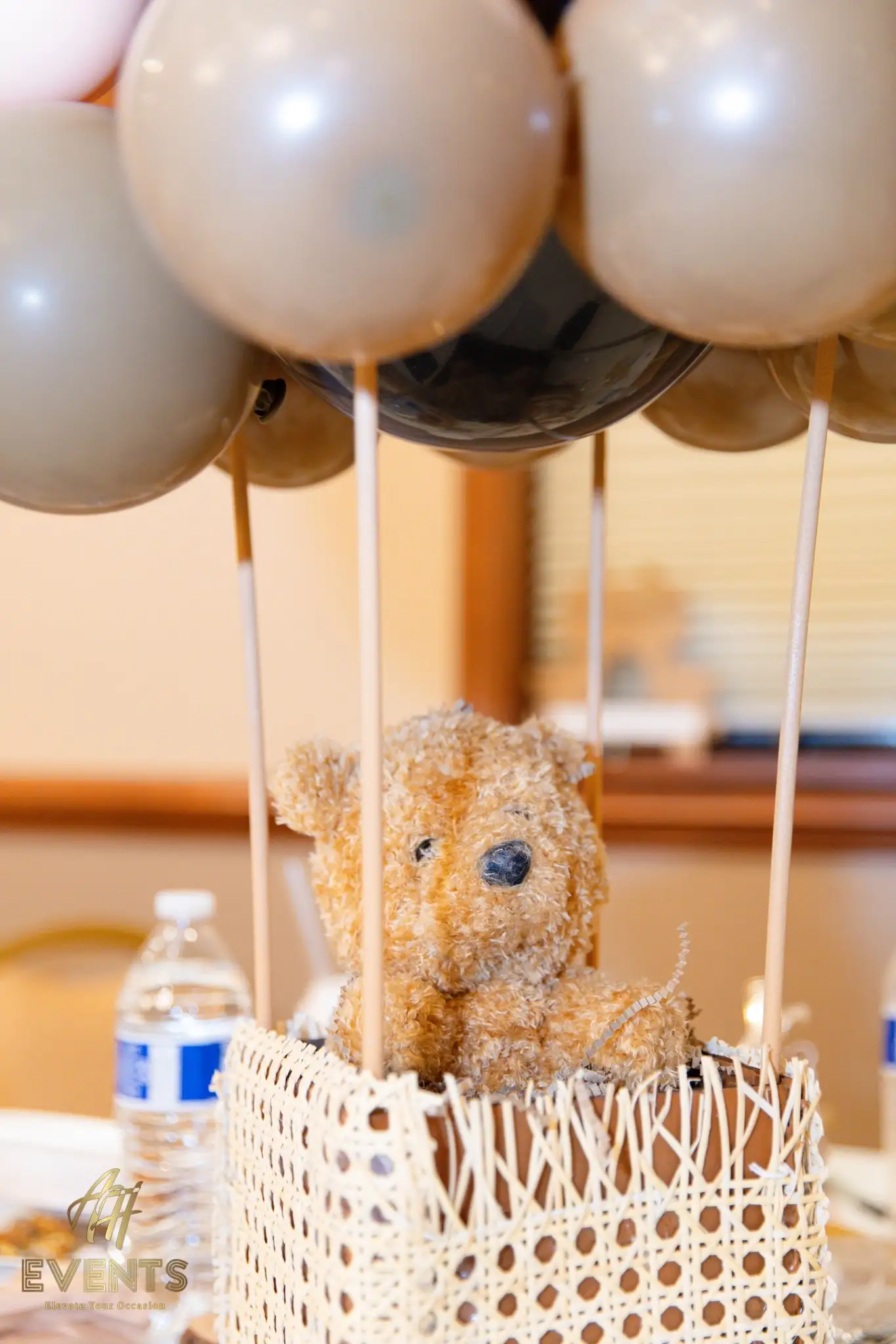 Hot-air-balloon centerpiece with a teddy bear in a woven basket beneath tan and black balloons