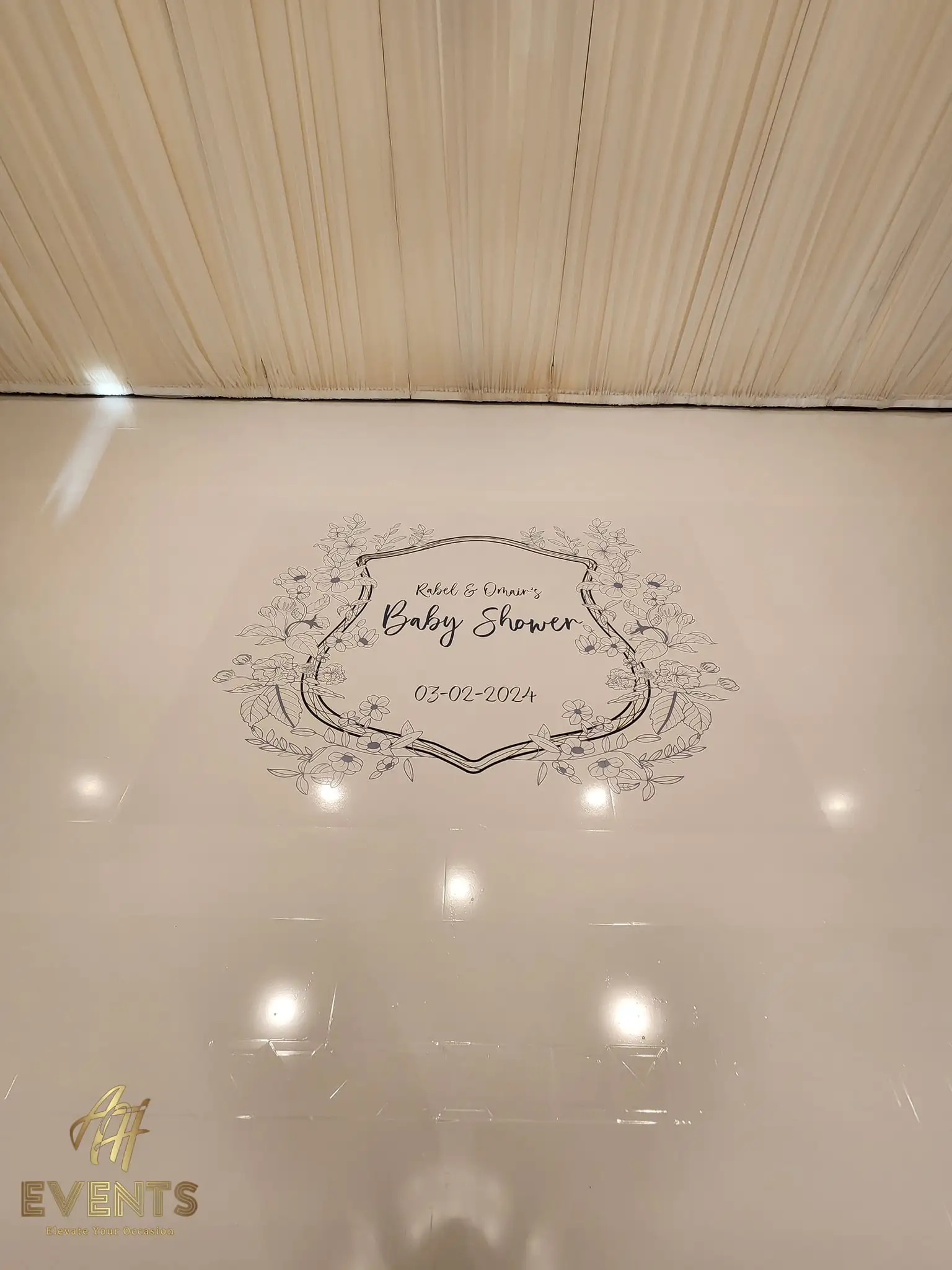 Close view of the 'Rabel & Omar's Baby Shower' floral-crest decal on the glossy cream dance floor