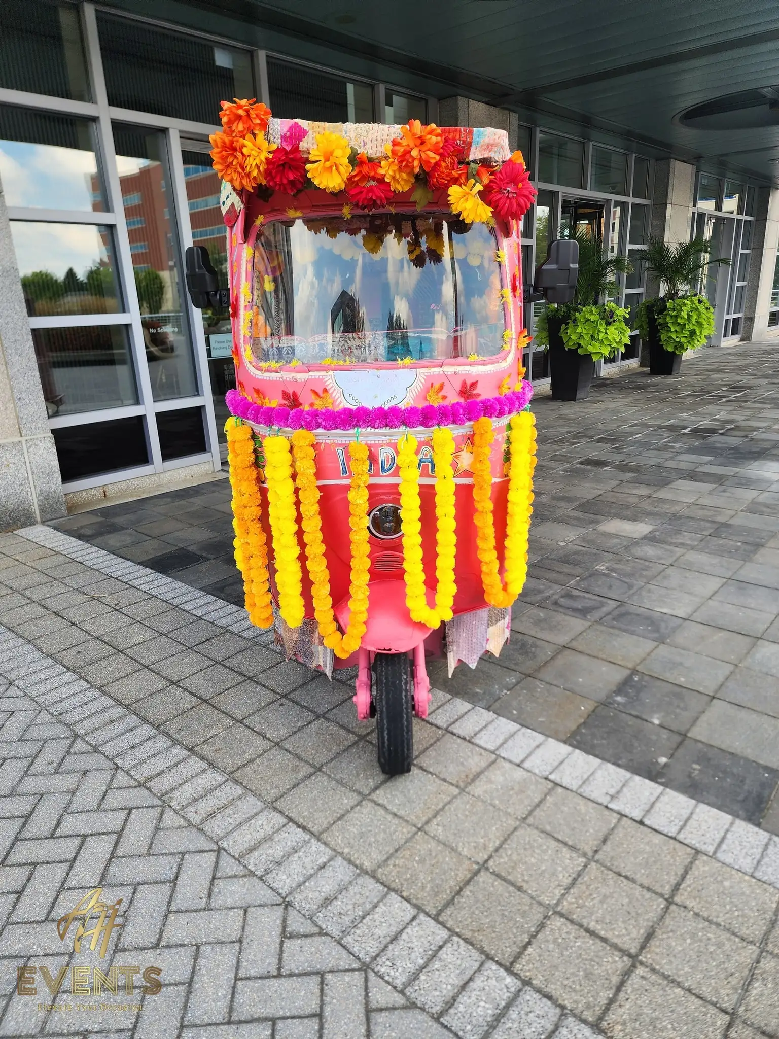 Front of the auto rickshaw with marigold garland curtains, parked at a building entrance