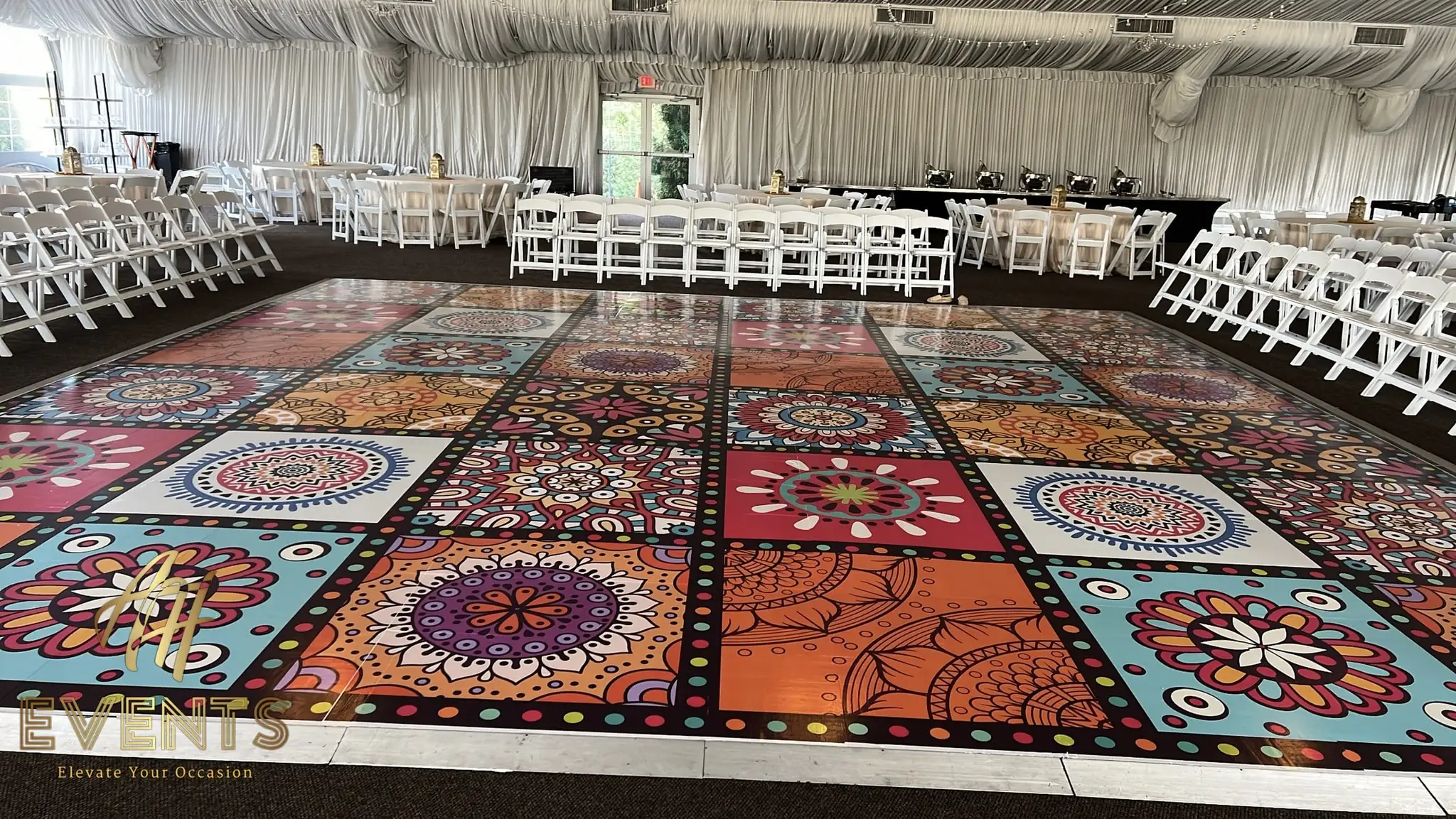 Wide view of the mandala-tiled dance floor among white folding chairs in a draped tent