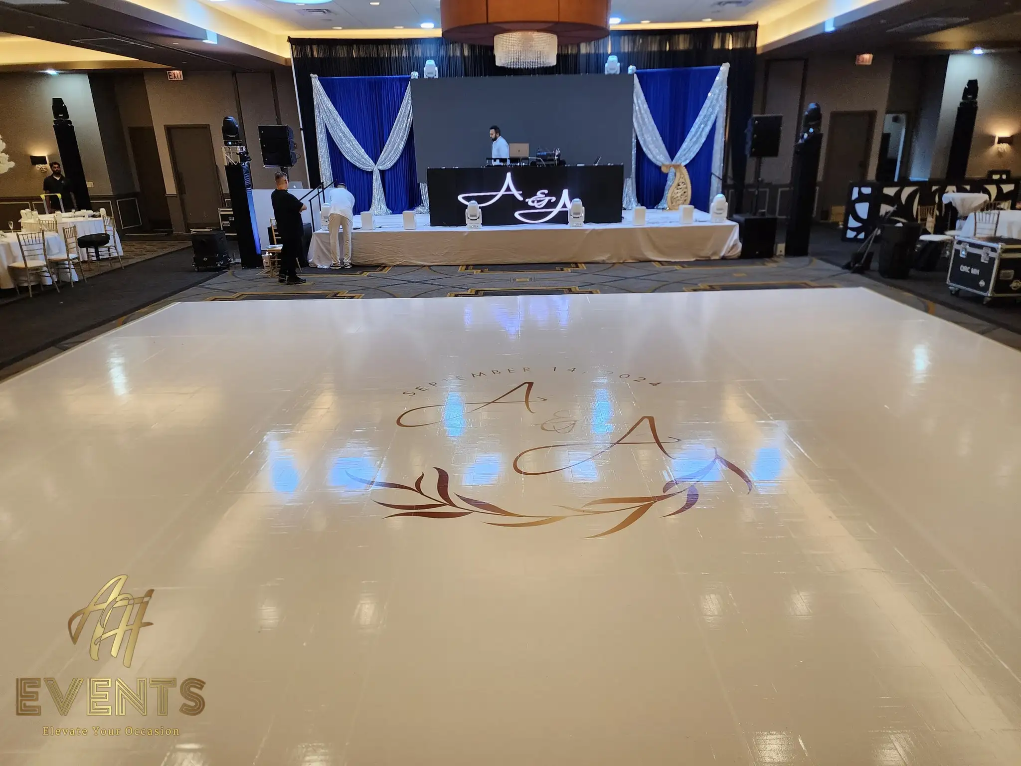 White dance floor with the 'A & A — September 14, 2024' monogram and foliage wreath, facing the navy DJ stage
