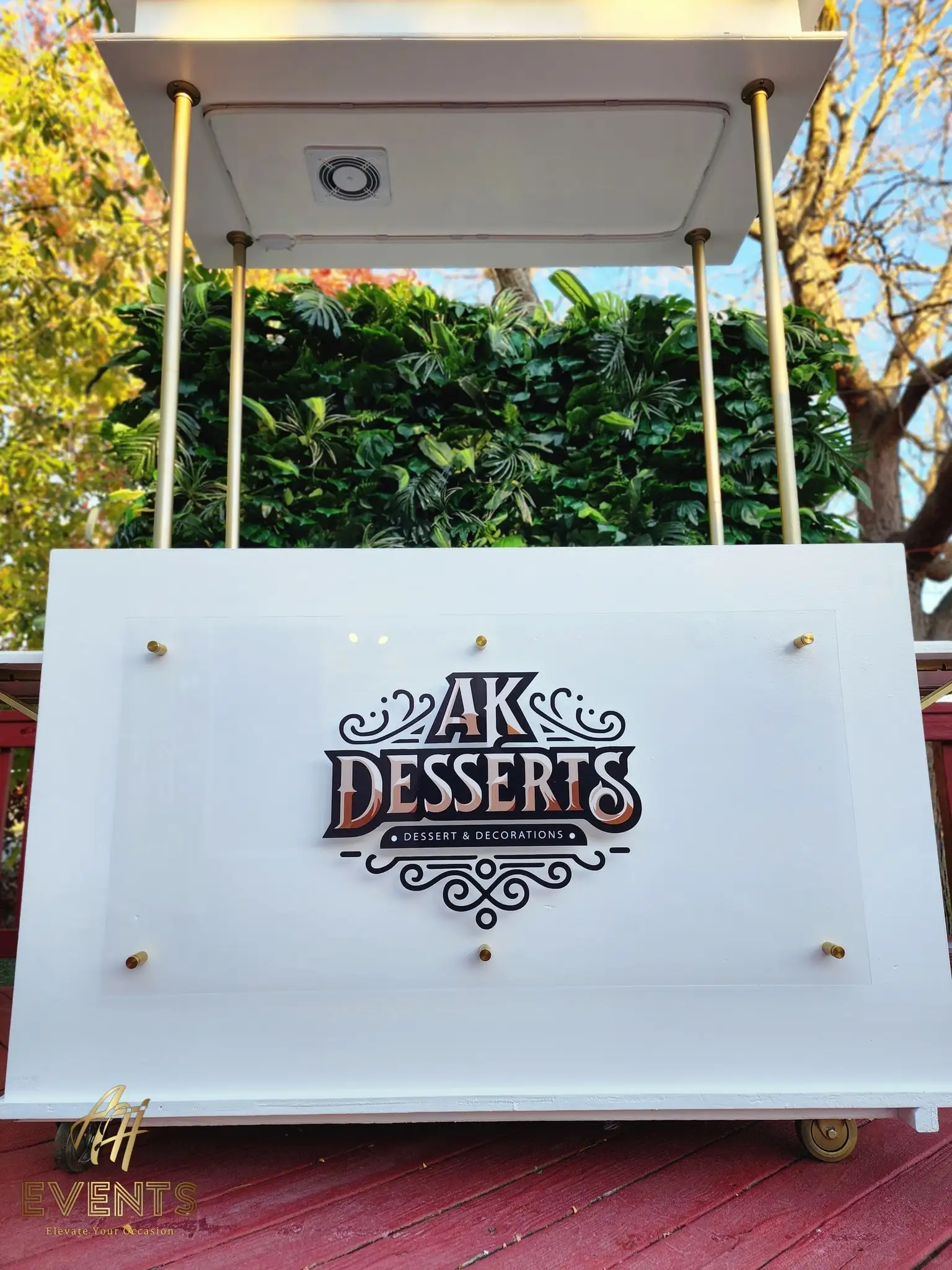 Front of the AK Desserts cart showing the acrylic logo panel mounted with gold standoffs and a canopy spotlight above