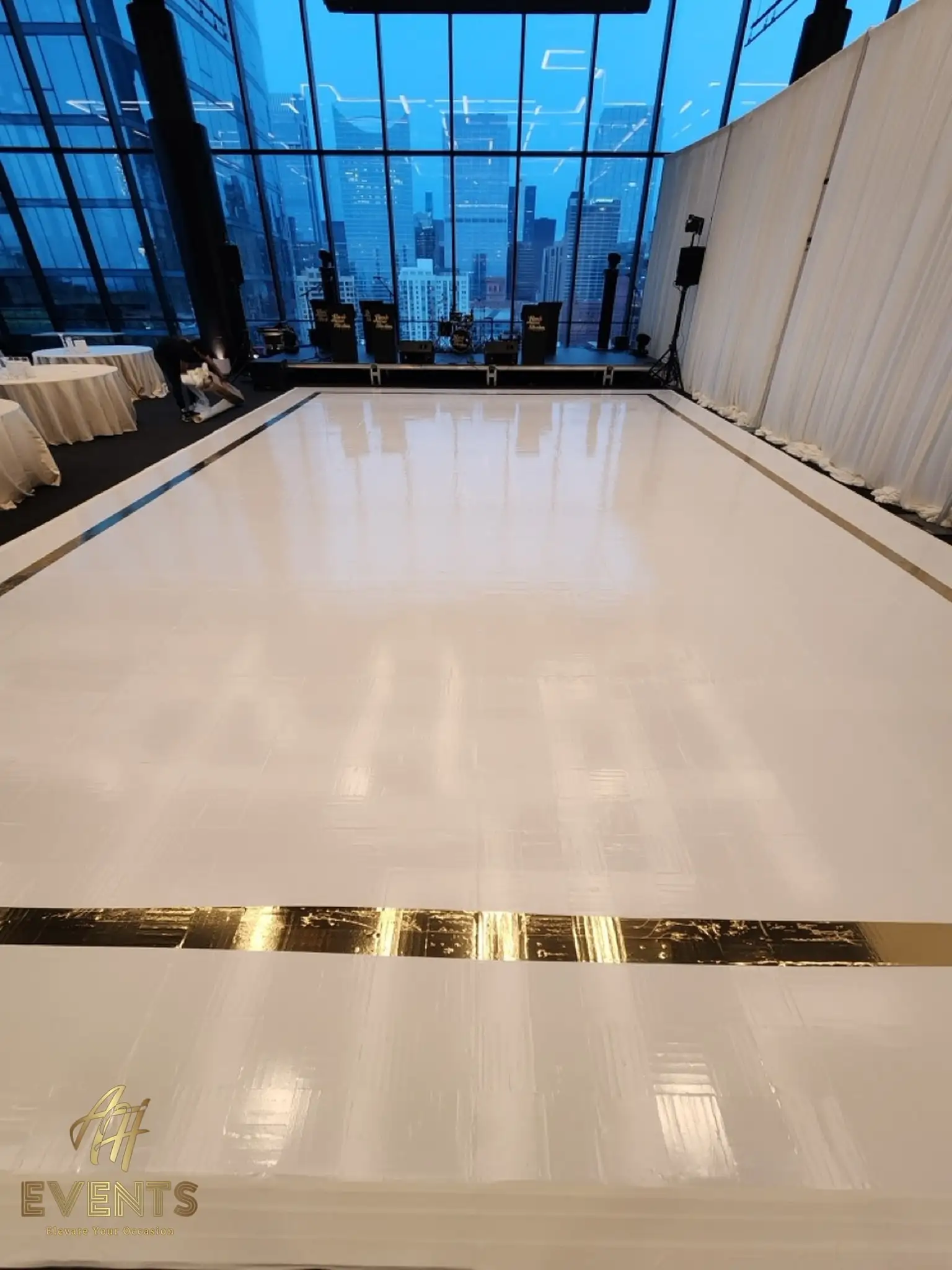White dance floor with a gold mirror border in the loft, a white pleated drape and skyline windows behind