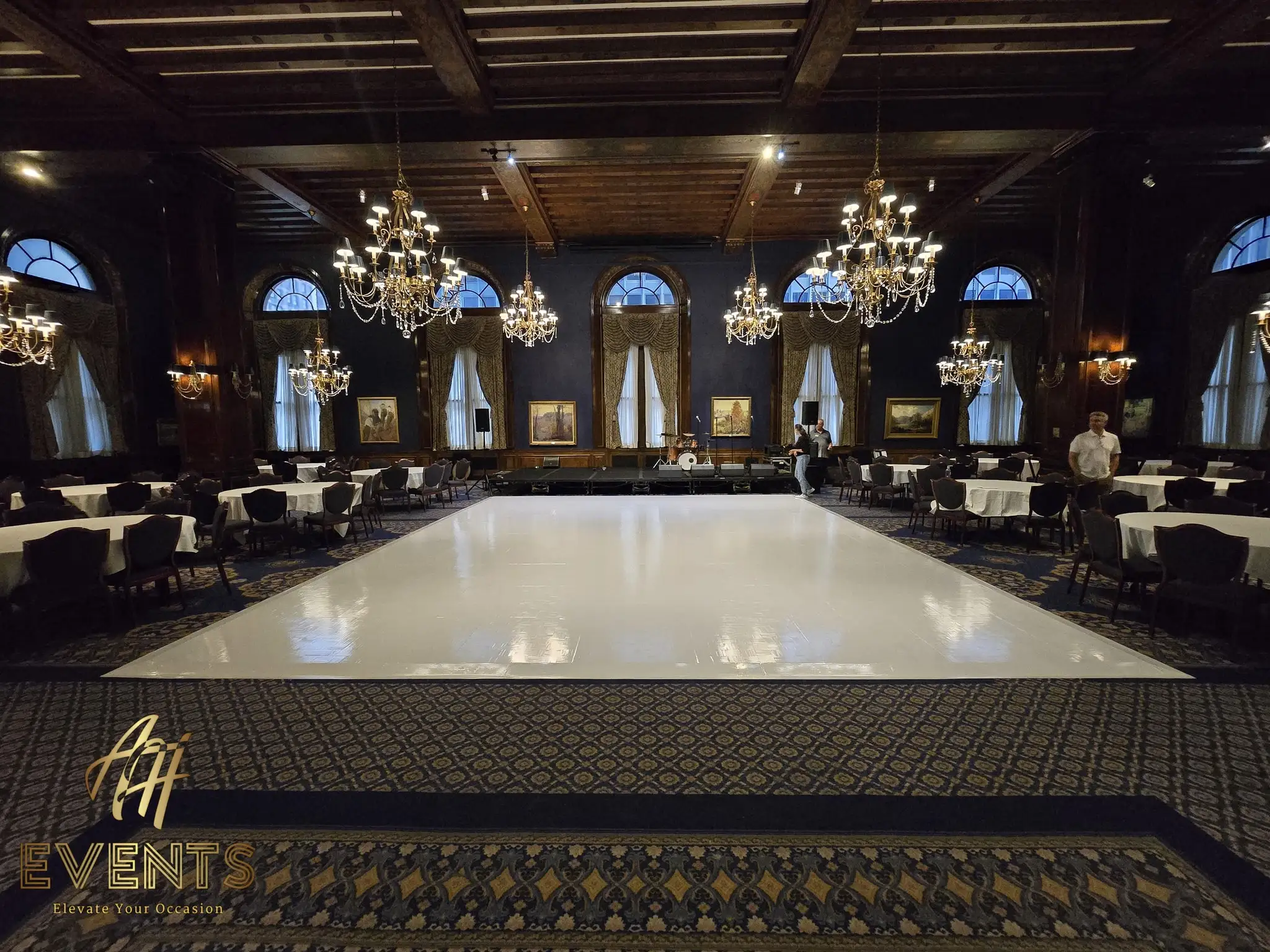 Glossy white dance floor in the navy wood-beamed ballroom, chandeliers and oil paintings around