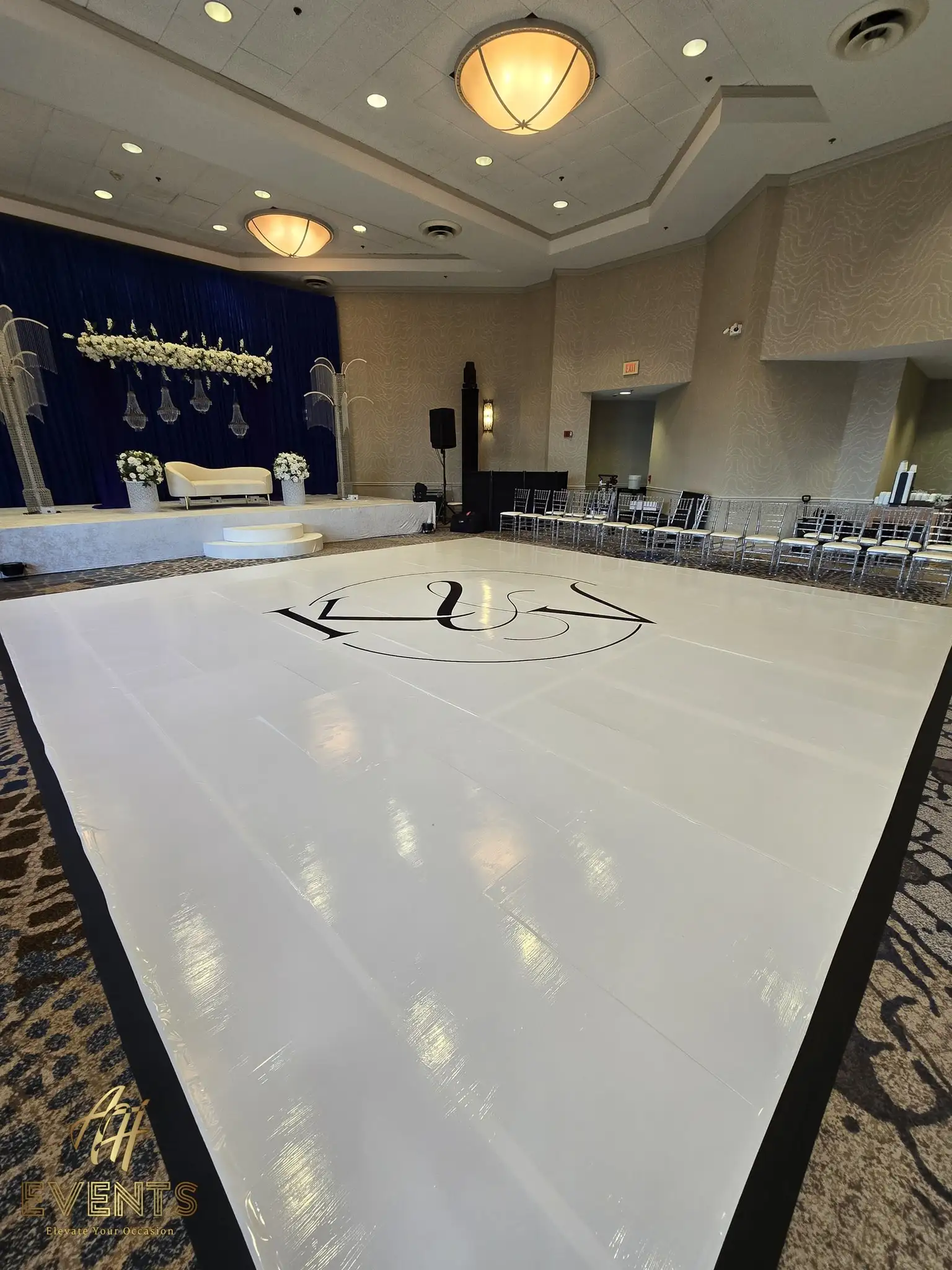 White 'K&V' monogram dance floor before a navy stage with crystal palm columns and a white sofa