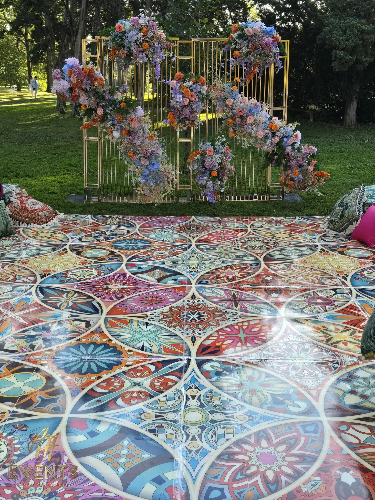 Close view of the Kaleidoscope floor outdoors, its circular mandala pattern catching the sun, with a floral arch behind