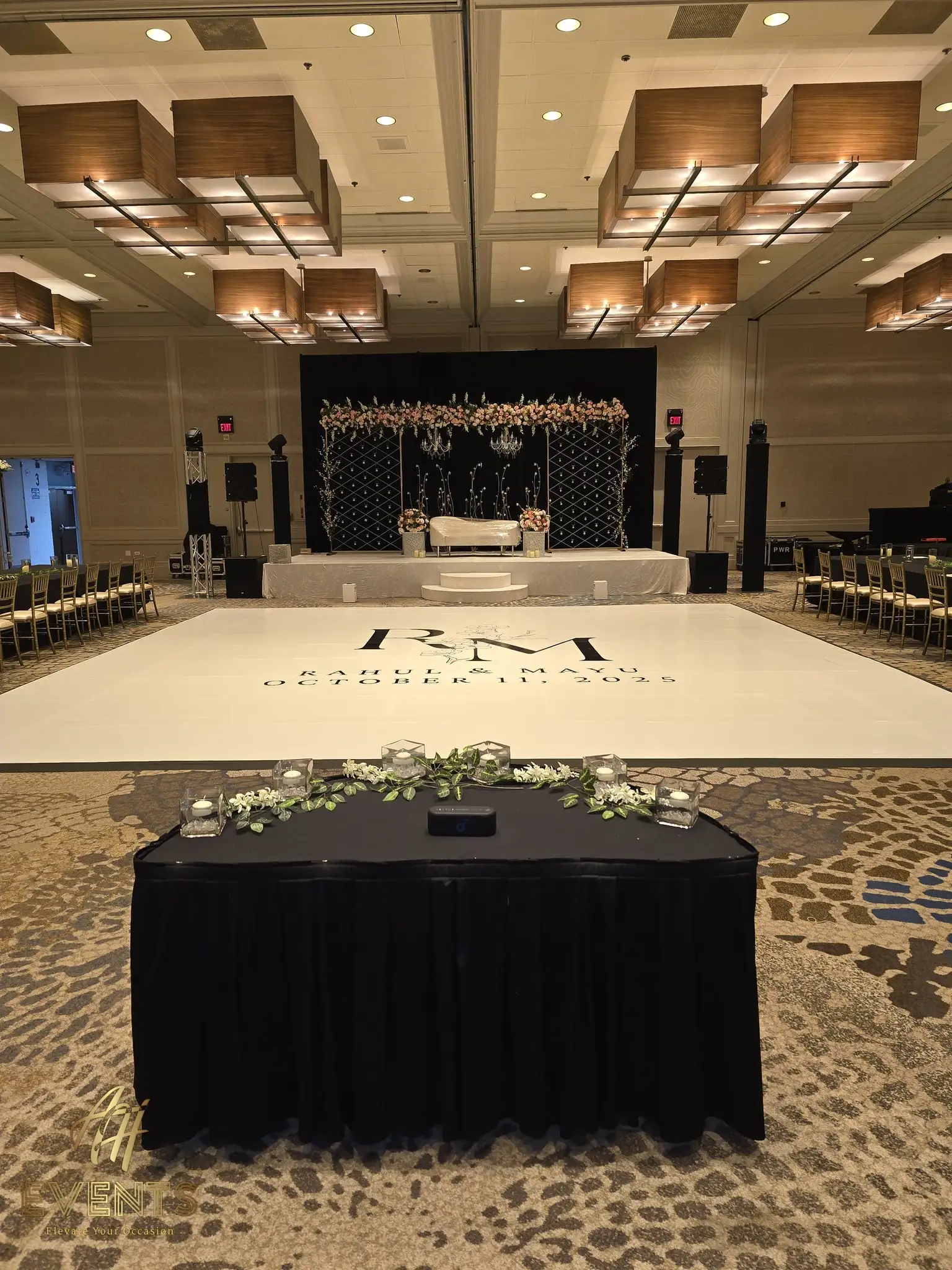 White 'R M' monogram dance floor with a black-draped head table and greenery garland in front