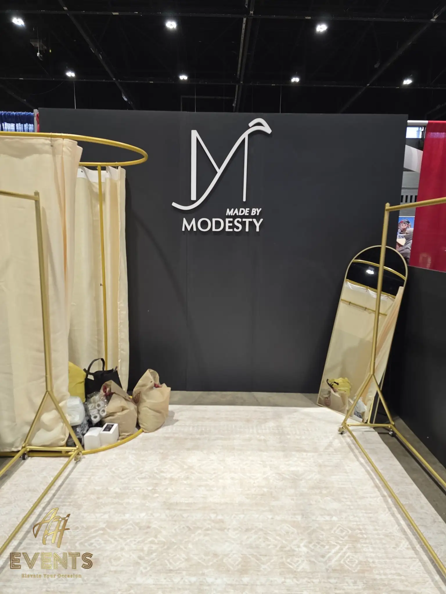 Made by Modesty booth with the logo wall, gold clothing racks and a standing mirror