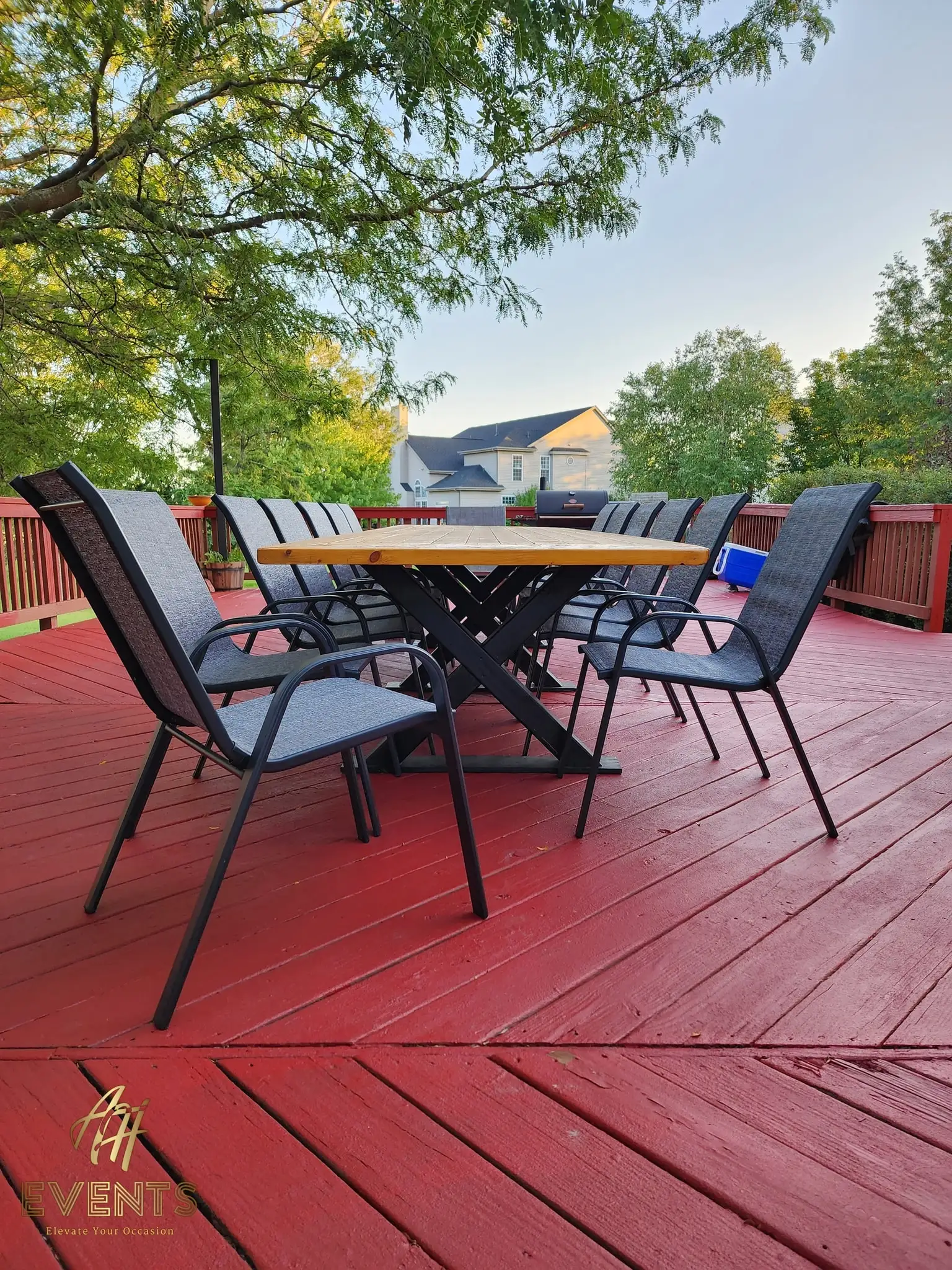 Smaller wooden table with black X-legs and six chairs on a red deck, neighborhood houses behind