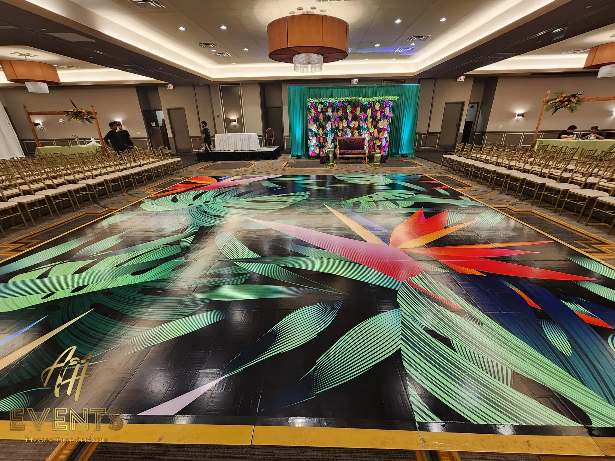 Wide view of the tropical leaf-art dance floor and teal stage lined with chairs