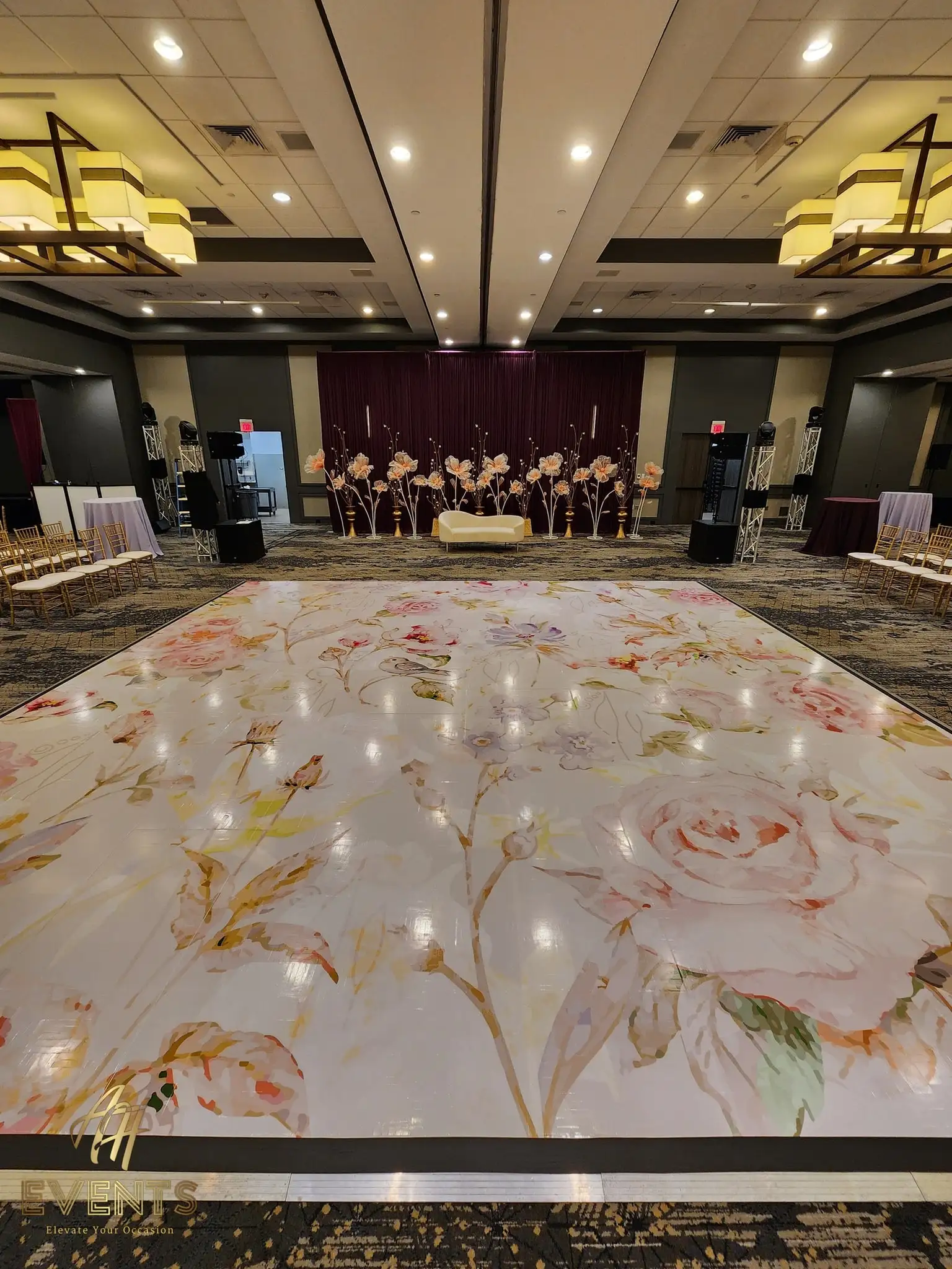 Wide view of the pastel floral dance floor in a ballroom with a floral backdrop and gold chairs