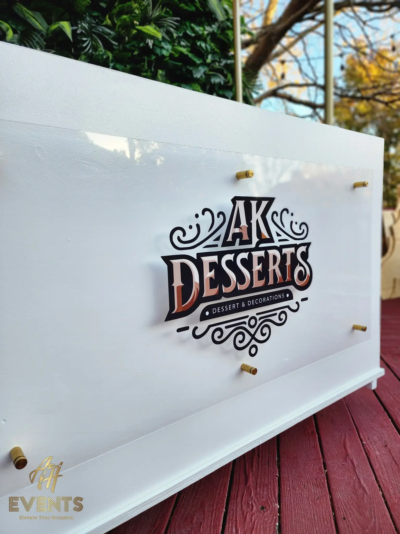 Close-up of the AK Desserts 'Dessert & Decorations' logo on the cart's white acrylic front panel with gold standoff bolts