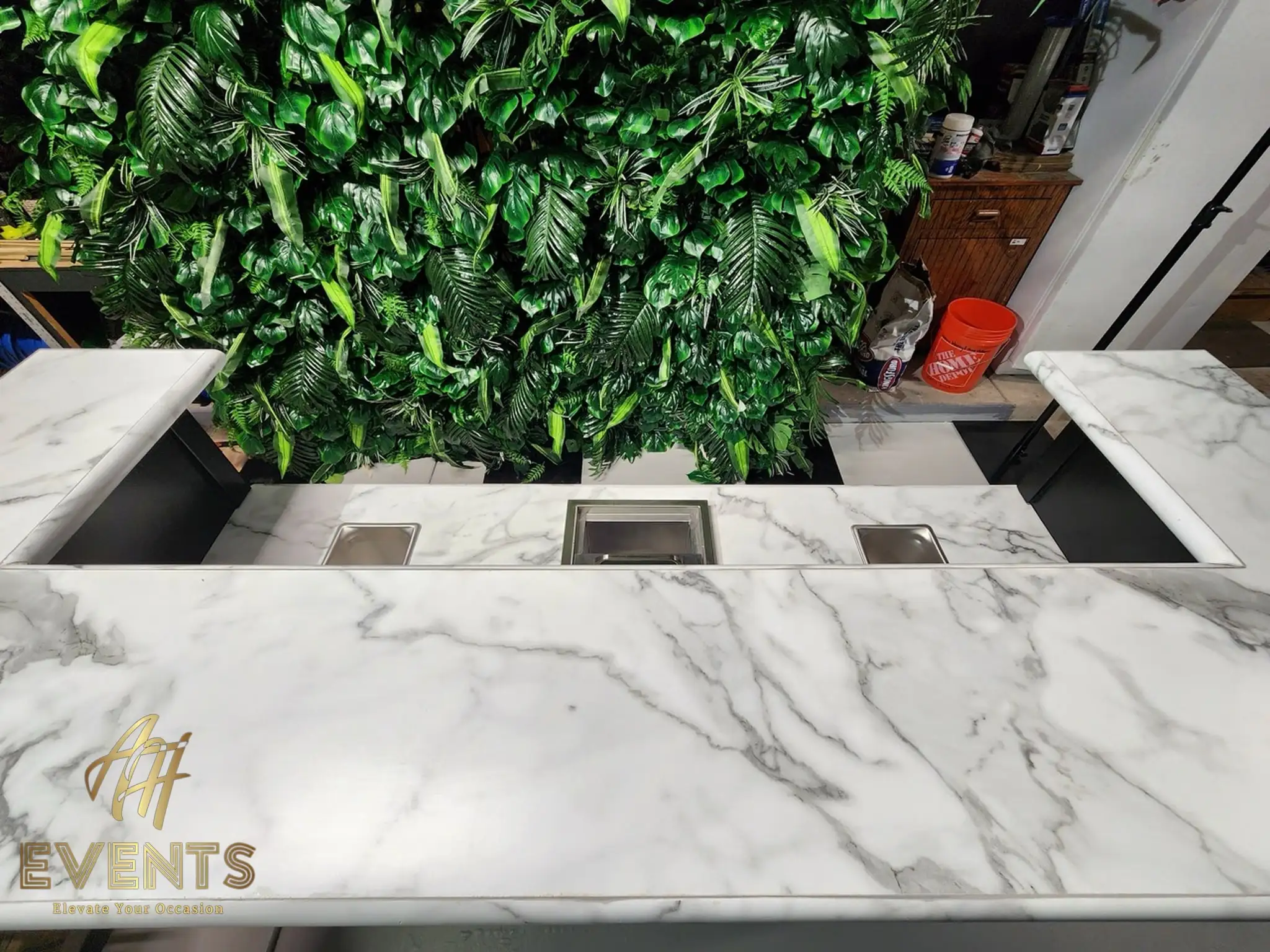 Top view of the Bobawala cart's marble counter with three stainless insets, a greenery wall behind in the workshop
