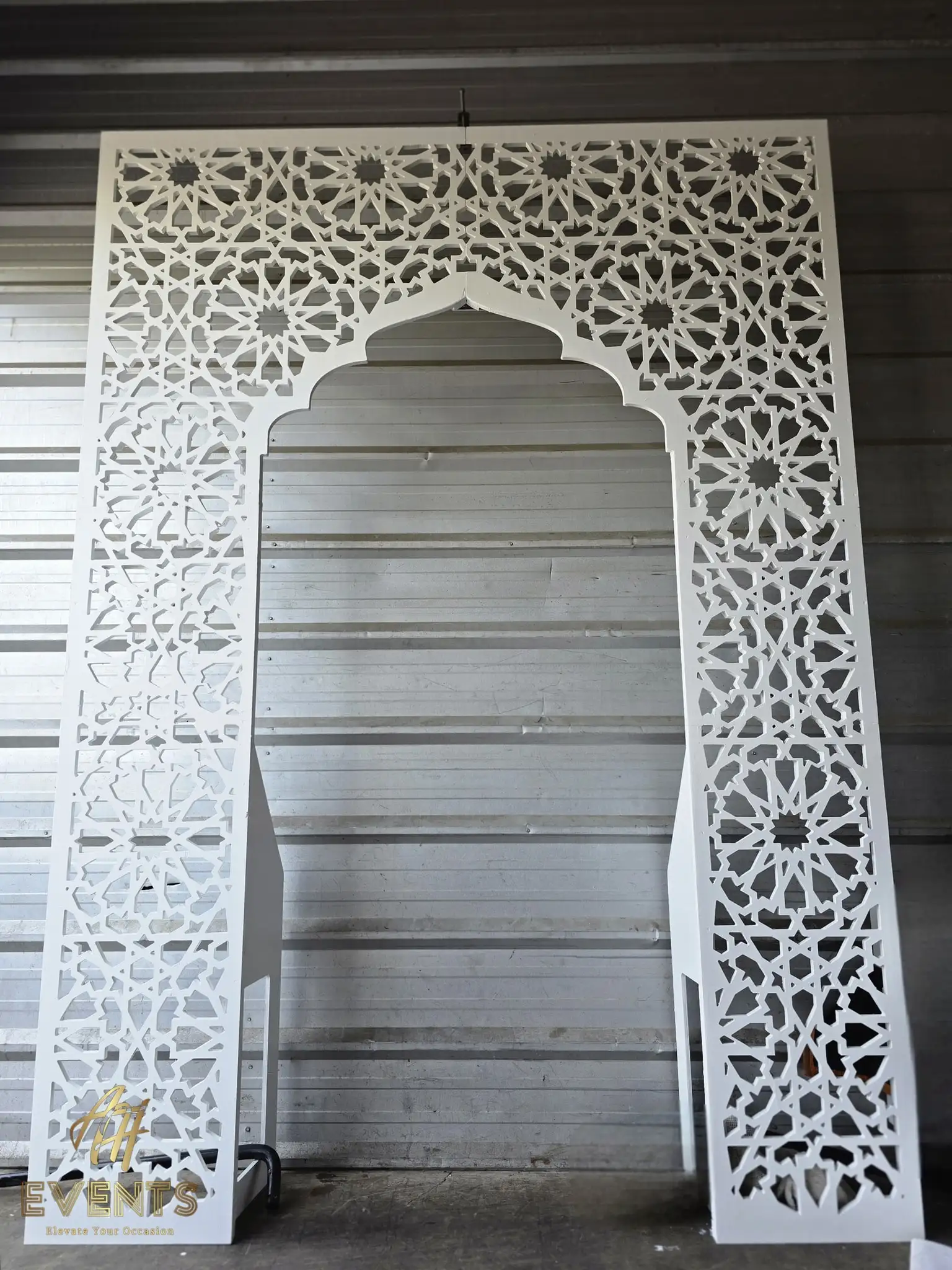 Full white semi-gloss matrix arch with a pointed Mughal opening against a metal workshop wall