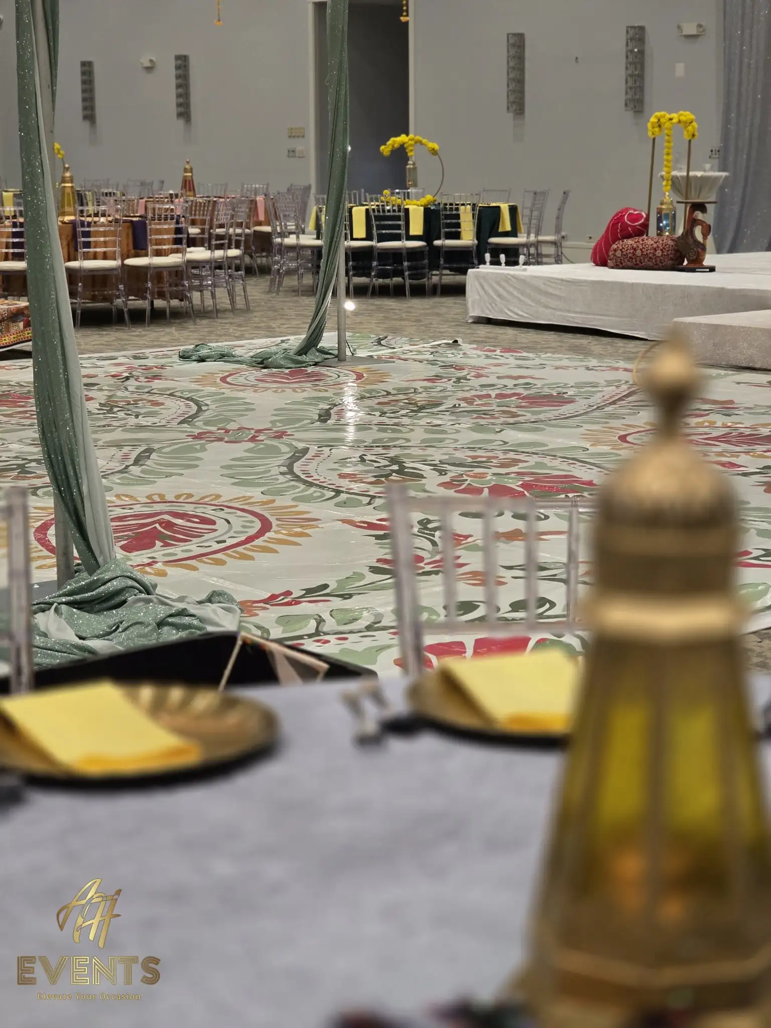 Floral flex vinyl floor viewed past a table setting with gold lanterns and charger plates at an indoor event