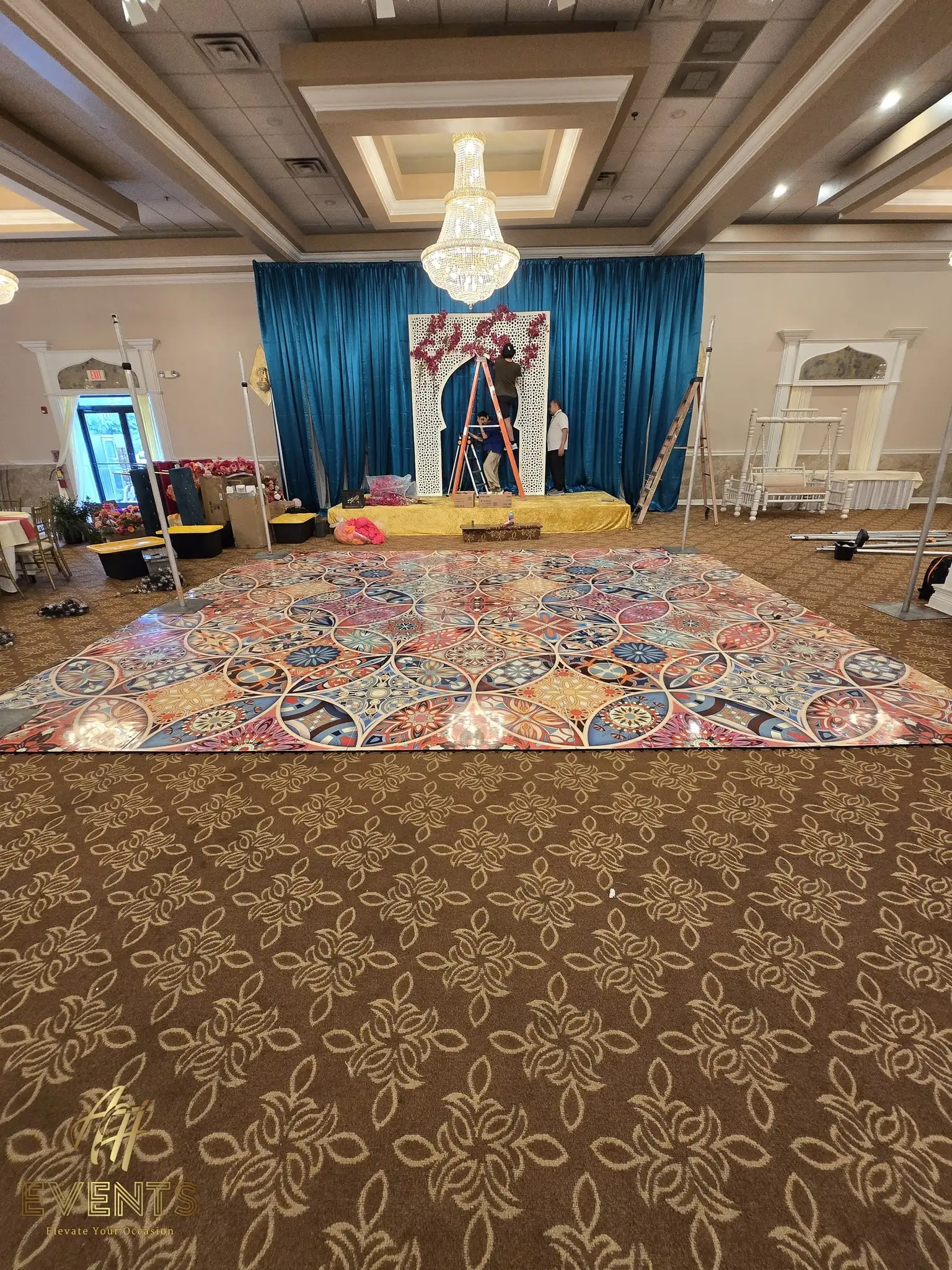 Kaleidoscope floor being installed in front of a teal-draped stage during event setup