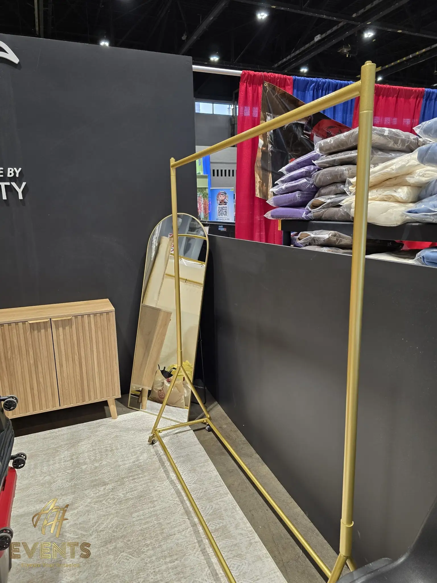Side view of the Made by Modesty booth with a gold rack and mirror beside neighboring convention booths