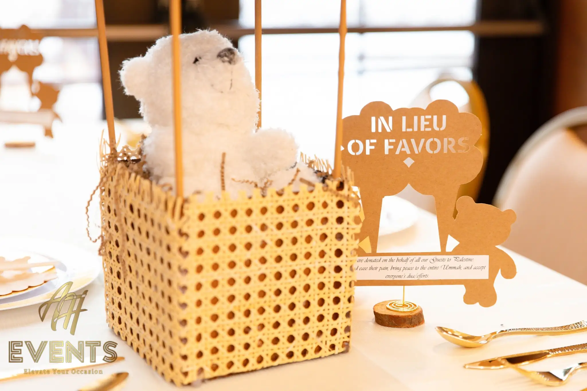 White teddy bear in a woven hot-air-balloon basket centerpiece beside the 'In Lieu of Favors' card