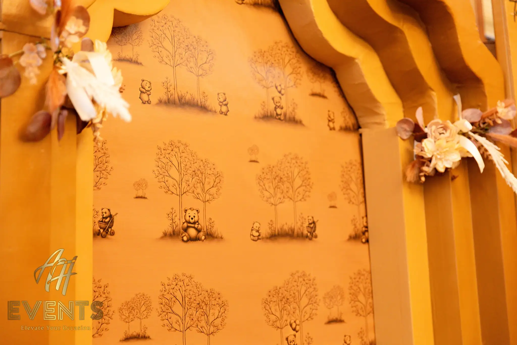 Detail of the gold arch backdrop with teddy-bear forest wallpaper and dried floral accents