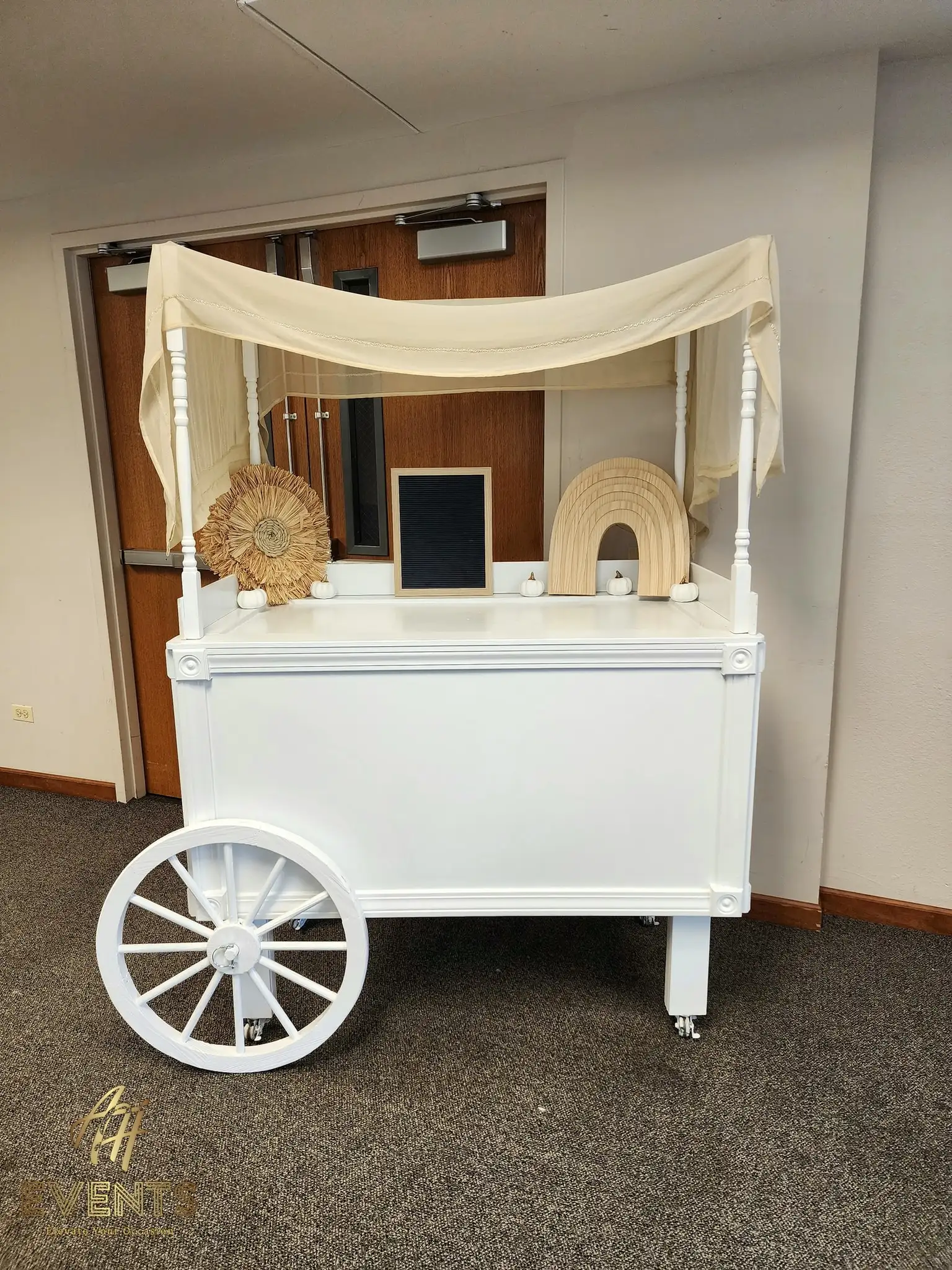 White favor cart draped with a cream canopy and styled with boho rattan decor props