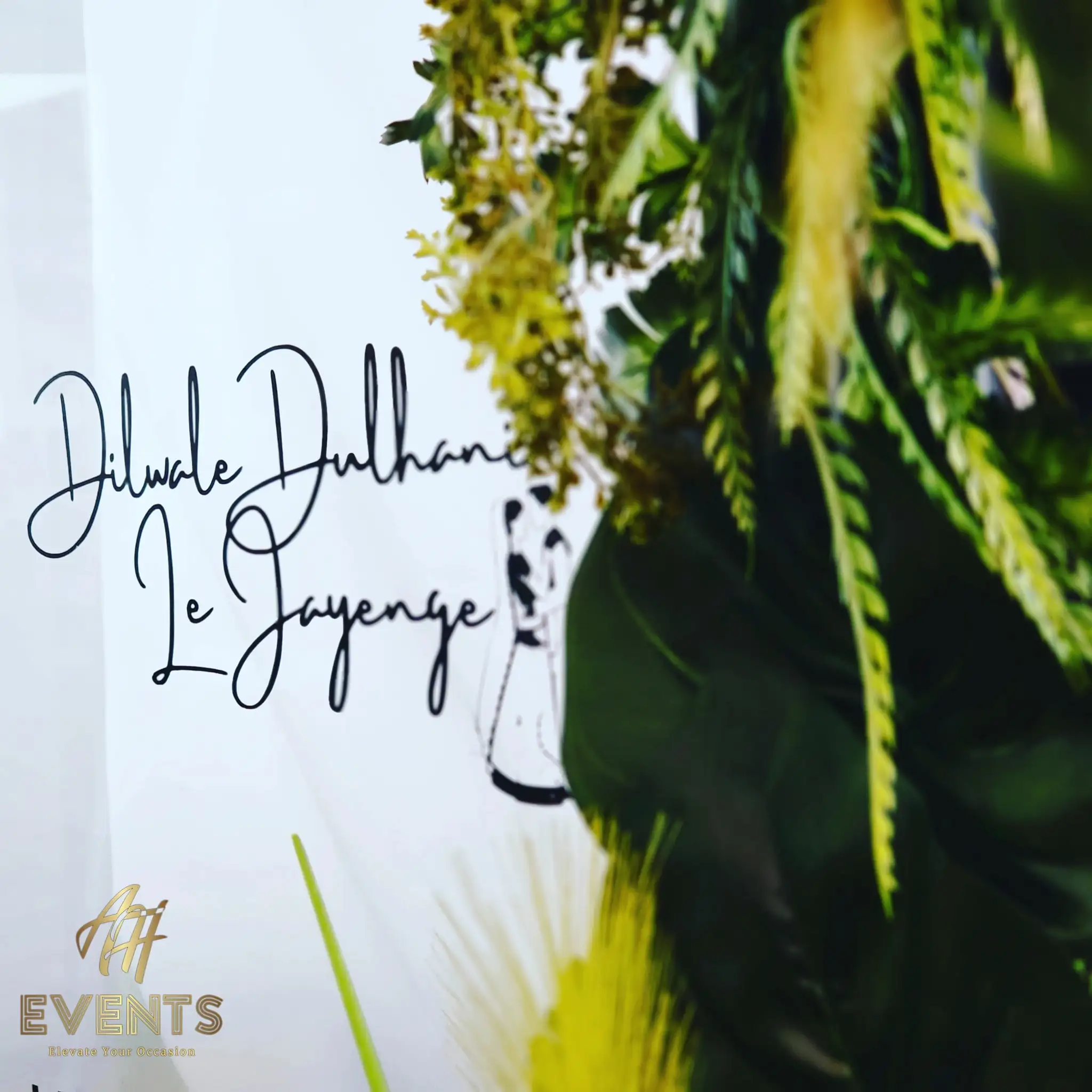 Photo-booth backdrop with 'Dilwale Dulhania Le Jayenge' script and a bride-and-groom illustration framed by greenery