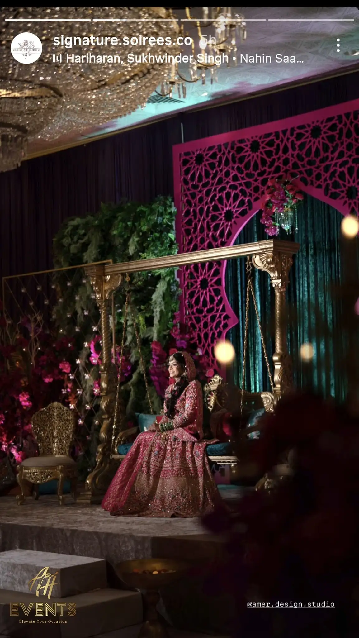 Bride on a gold swing in front of the pink matrix arch backdrop with cascading greenery and chandeliers at a reception