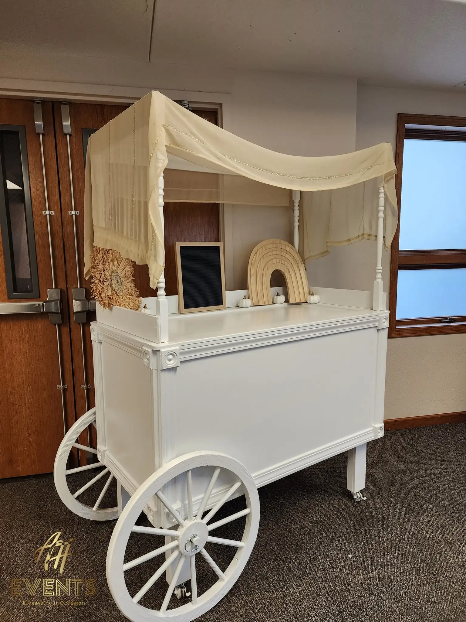 White canopy favor cart styled with pampas and a wooden rainbow on a dark carpet