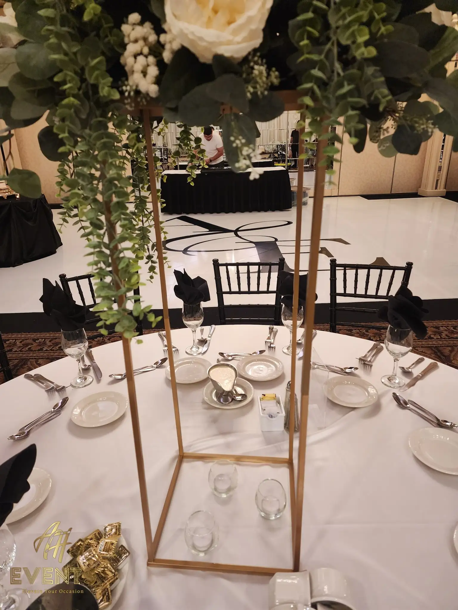 Gold-frame floral centerpiece on a round table beside the white 'A&E' monogram dance floor