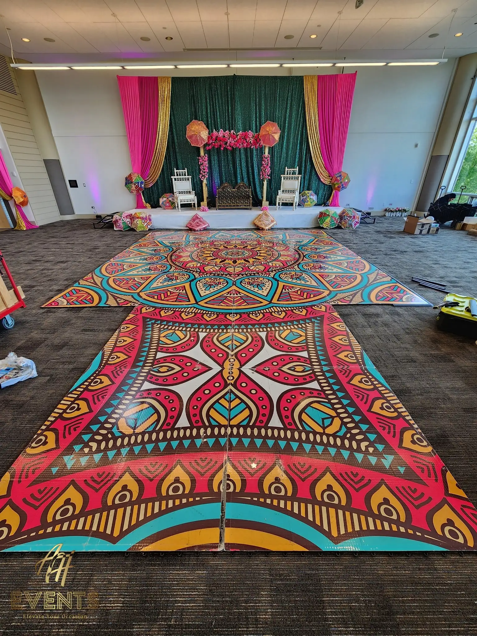Two mandala floor sections in a hall facing a green-and-pink draped stage with gold seating